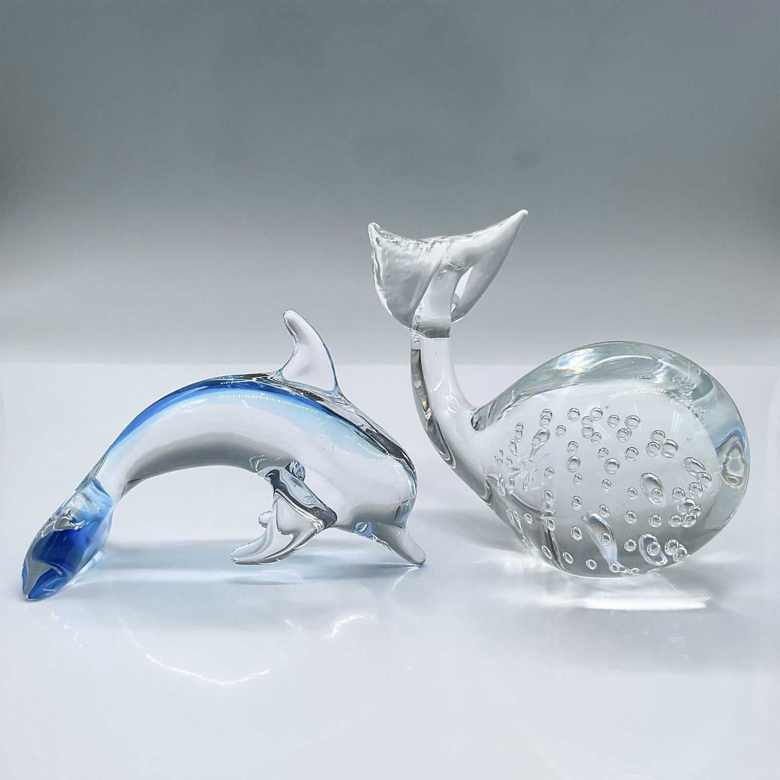 2pc Crystal Dolphin and Whale Paperweights: Features a Sardinia Crystal clear blue dolphin paperweight and clear whale paperweight. Largest measures 4.75"L x 2.5"W x 4"H. The dolphin has a Sardinia Crystal Sticker. Dimensions: See Description