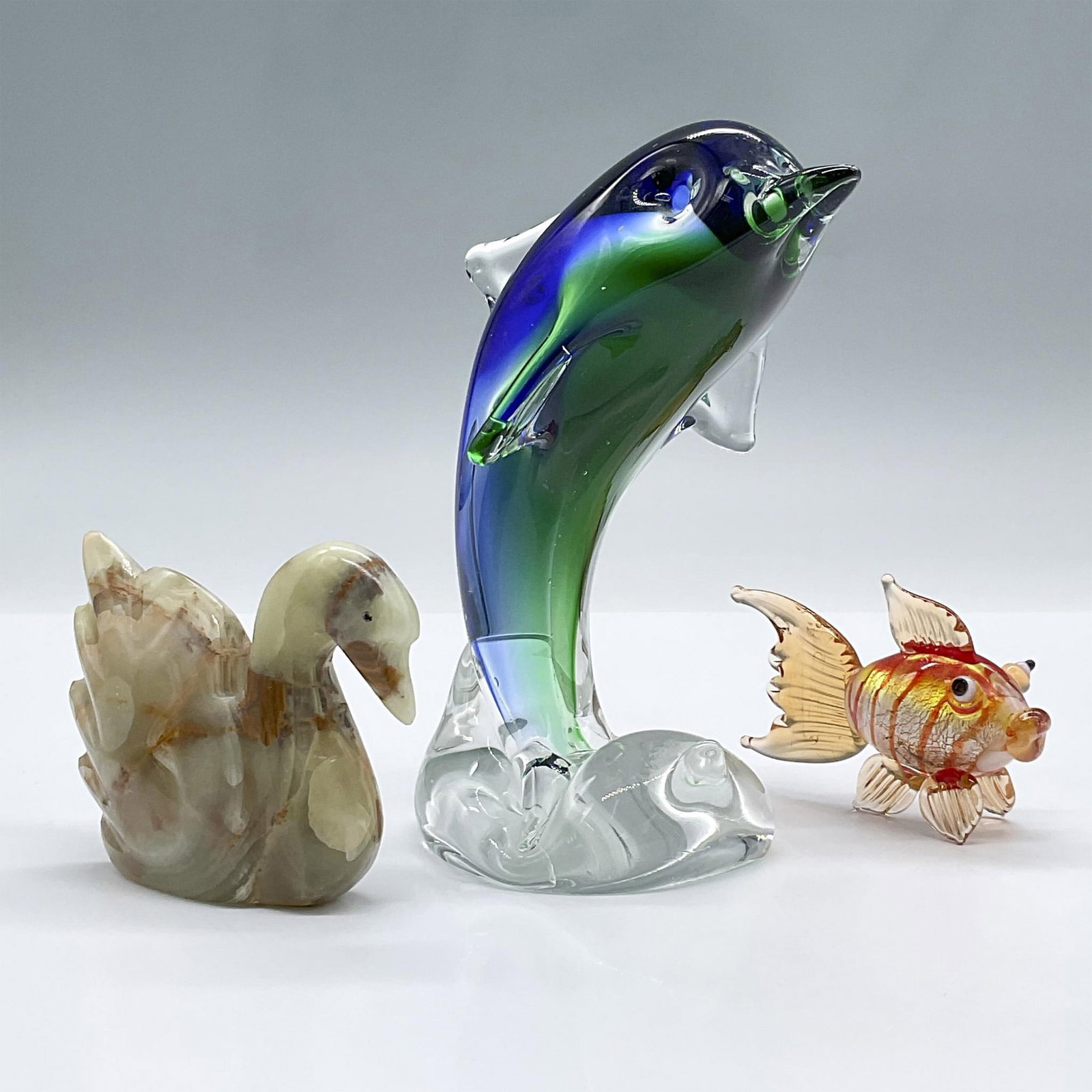 3pc Art Glass and Onyx Figurines: Includes two lovely art glass marine creatures, a dolphin and goldfish, and a sleek green onyx carved swan. Largest measures 4"L x 3"W x 5.75"H. Issued: 20th century Dimensions: See Description