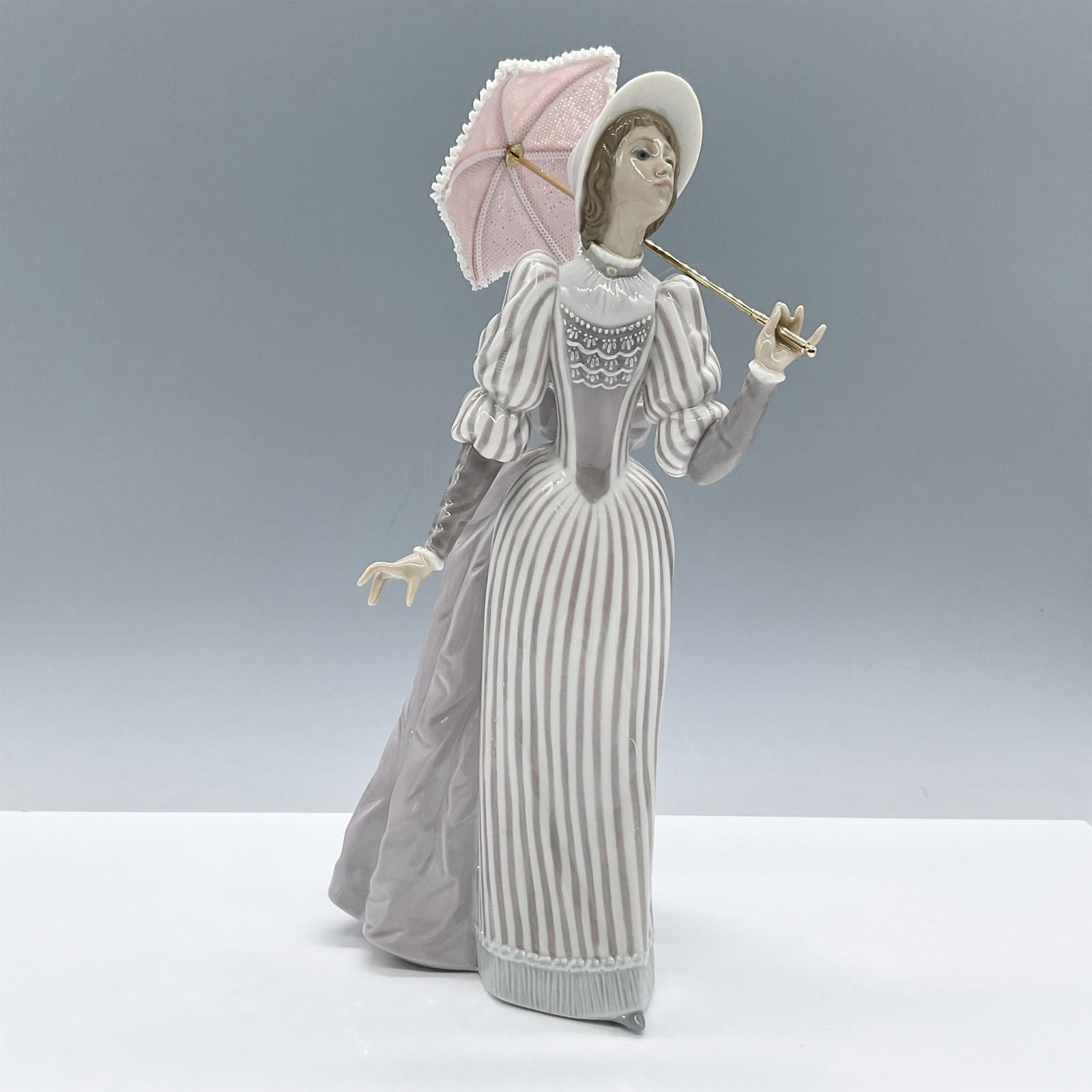 English Lady 1005324 - Lladro Porcelain Figurine: Glossy finish figure modeled as an English lady peering in the distance as she holds a small parasol. Lladro backstamp. Artist: Jose Puche Issued: 1985-1994 Dimensions: 5.25"L x 4.5"W x 10.75"H Manufa