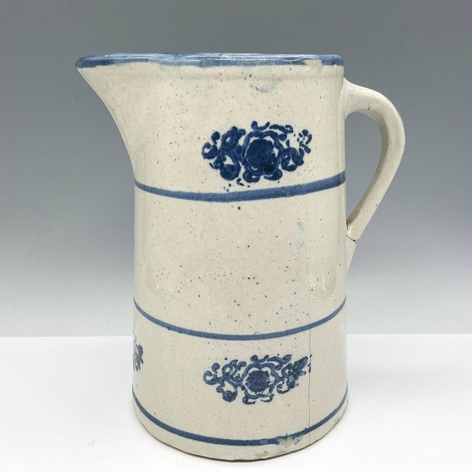 Vintage Wildflower Stoneware Pitcher: Natural thrown pottery with wildflowers and banding colored in blue. Issued: 20th century Dimensions: 8"L x 5"W x 8.75"H