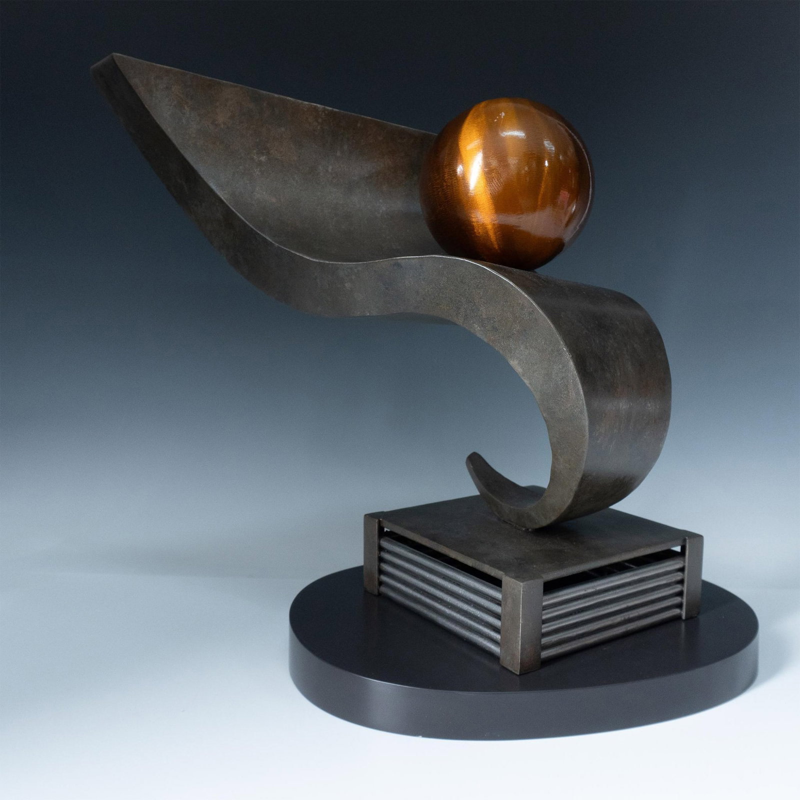 Eugene Perry Metal Art Sculpture and Base, Atlas: Eugene Perry is an award-winning abstract metal sculptor from Philadelphia who was a mentee of Jung Park. This piece titled Atlas is a captivating stainless-steel sculpture with a striking orange sphe