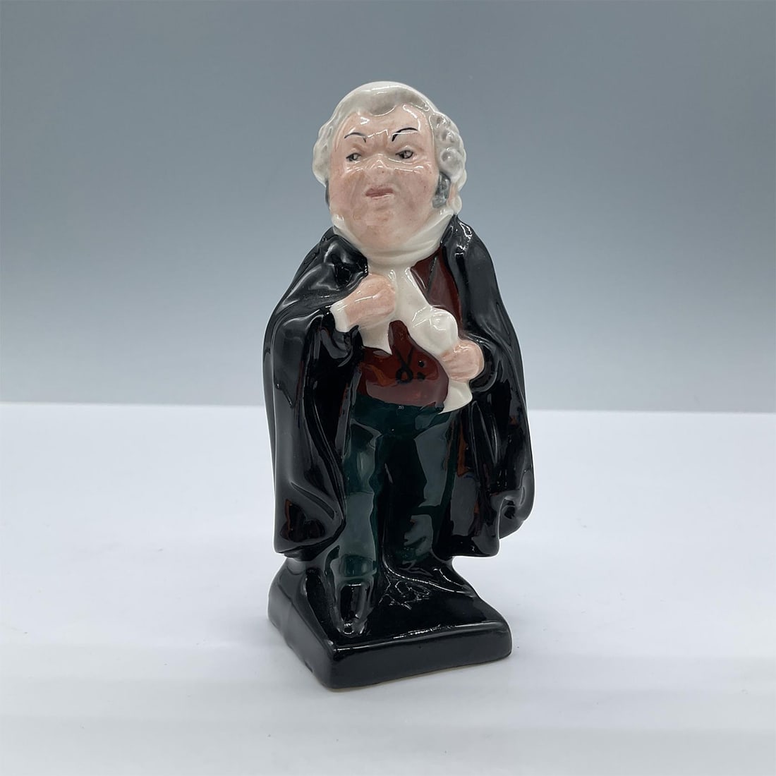 Royal Doulton Dickens Character Figurine, Buzfuz: From the Charles Dickens Series. Modeled in black, white, maroon and green colors with a glossy finish. Royal Doulton backstamp. Issued: 20th century Dimensions: 2.25''L x 1.75''W x 4.5''H Manufacture