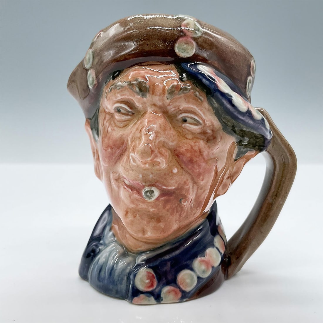 Blue D6235 - Small - Royal Doulton Character Jug: First original version of the Pearly Boy in a blue coat with colorful pearly buttons. Royal Doulton backstamp. Artist: Harry Fenton Issued: c. 1940 Dimensions: 3''L x 2.75''W x 3.25''H Manufacturer: R