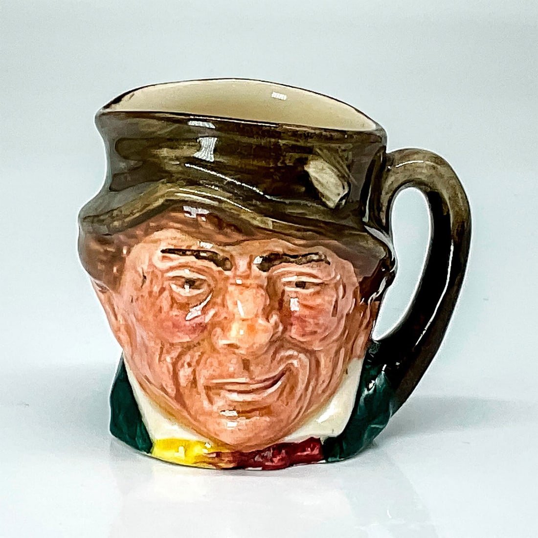 Paddy D6042 - Mini - Royal Doulton Character Jug: Brown hat; green coat; yellow and red scarf. Paddy, a colloquial term for an Irishman, is derived from St. Patrick, the country's patron saint. This gent is dressed in traditional green for St. Patric