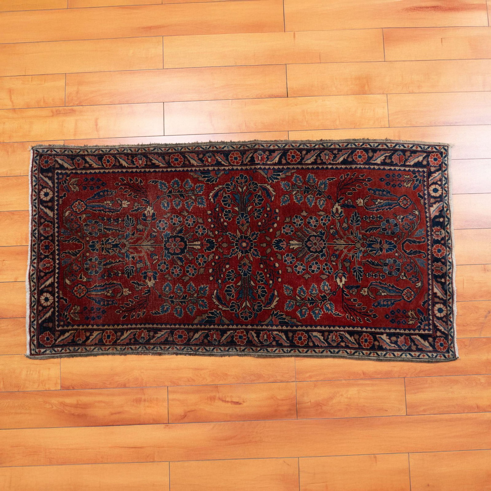 Persian Red Sarouk Hand Knotted Rug: A rectangular red rug adorned with a blue border, featuring beautiful flowers scattered throughout the design in shades of red, blue, and white. Dimensions: 58.5"L x 30"W x 0.25"Pile Height