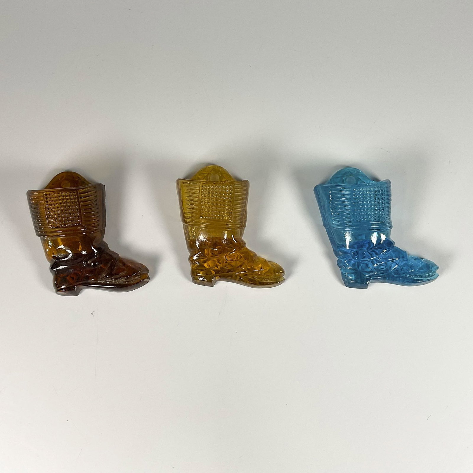 3pc Vintage Colored Glass Boot Wall Pockets: Brown, amber, and blue glass wall pockets designed to hold matches or pens, featuring intricate glass cut designs. Dimensions: 3.75"L x 1.75"W x 4.25"H