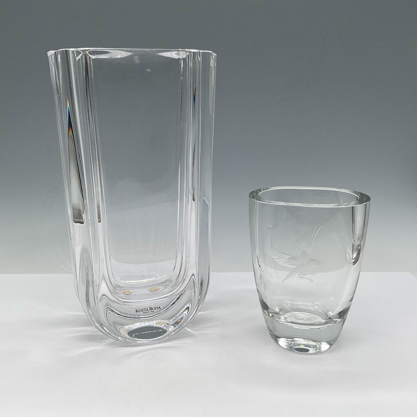 2pc Kosta Boda Goran Warff Crystal Vase + Etched Bud Vase: Lot includes glass vase architectural design with fluted sides and rounded base - 4.75"L x 3"W x 8.75"H - Kosta Boda G. Warff etched mark. Crystal bud vase with etched bird design - 3.5"L x 2.5"W x 4.