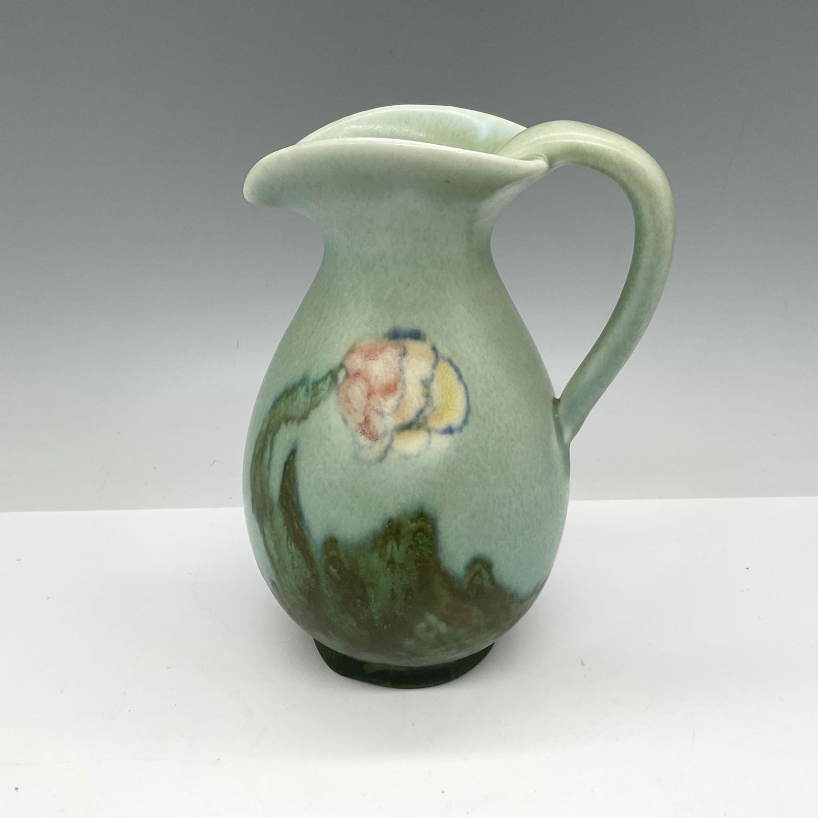 Rookwood Pottery Pitcher by John Wesley Pullman 2975: Soft mat pastel color of aqua with green, yellow and peach on floral design. Rookwood impressed mark. 2975. Artist monogram on base. Artist: John Wesley Pullman Issued: 1929 Dimensions: 4"L x 3.25"W x