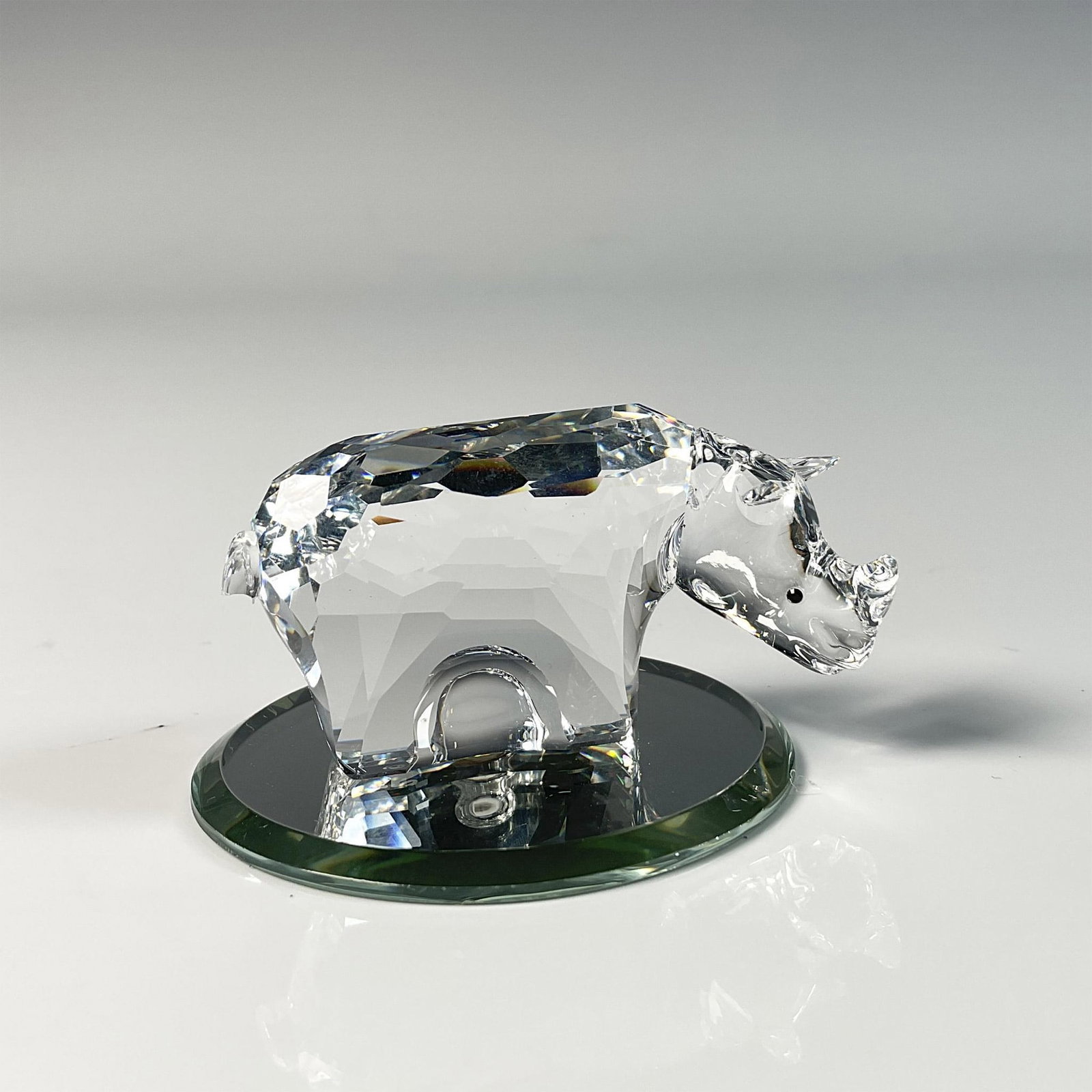 Swarovski Crystal Figurine and Base, Rhinoceros: Stunning figure featuring rhinoceros with an intricate cut design crafted from clear crystal. This item has a round mirror base included: 0.25"H x 2" dia. Original box: 3.25"W x 3.75"H. Outer Sleeve: 
