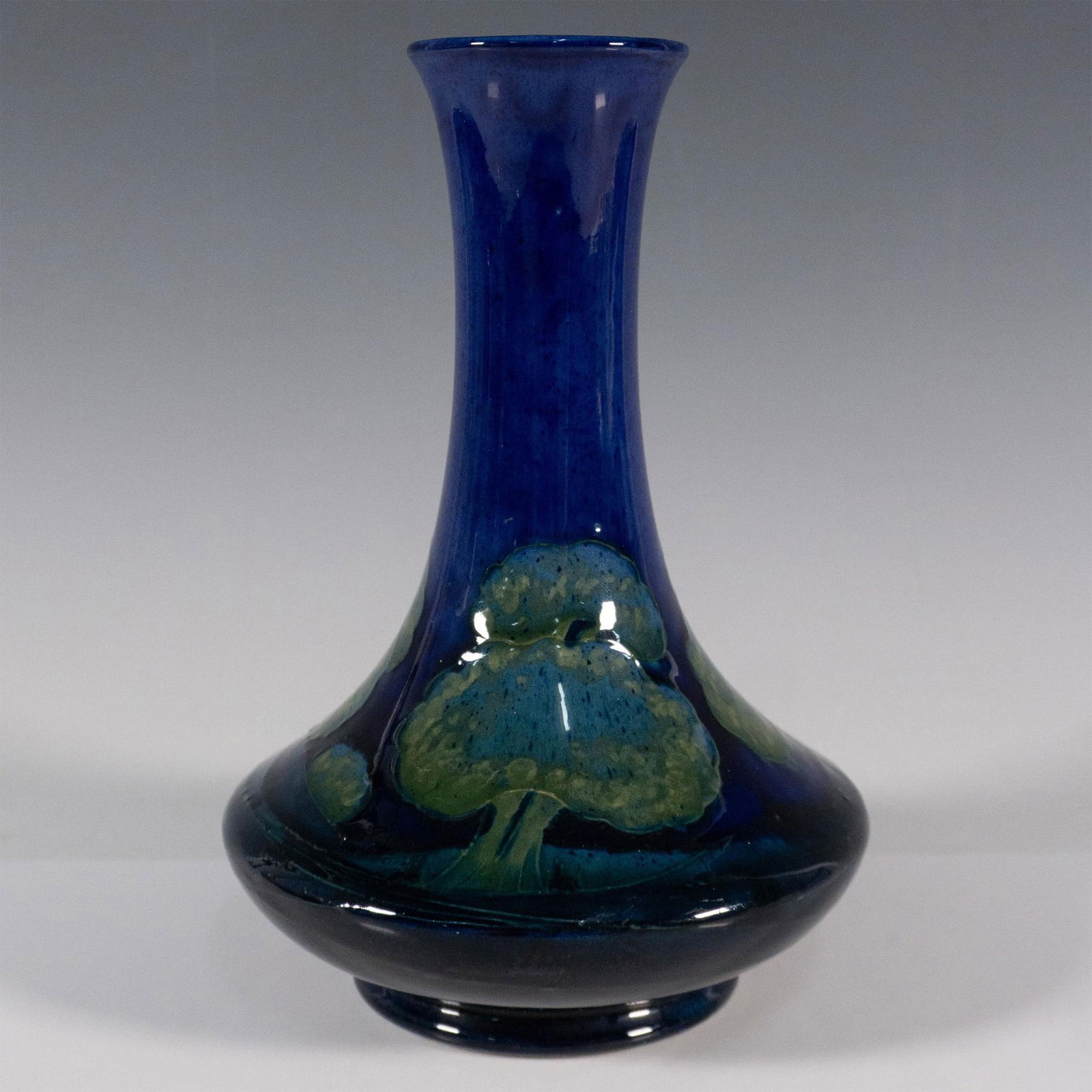 Moorcroft Pottery Vase Moonlit Blue: A squatted flower vase with a long neck. Hand painted cobalt blue glaze with green-blue tree. Moorcroft impressed marked. Issued: 20th century Dimensions: 5.25"L x 7.75"H Manufacturer: Moorcroft Count