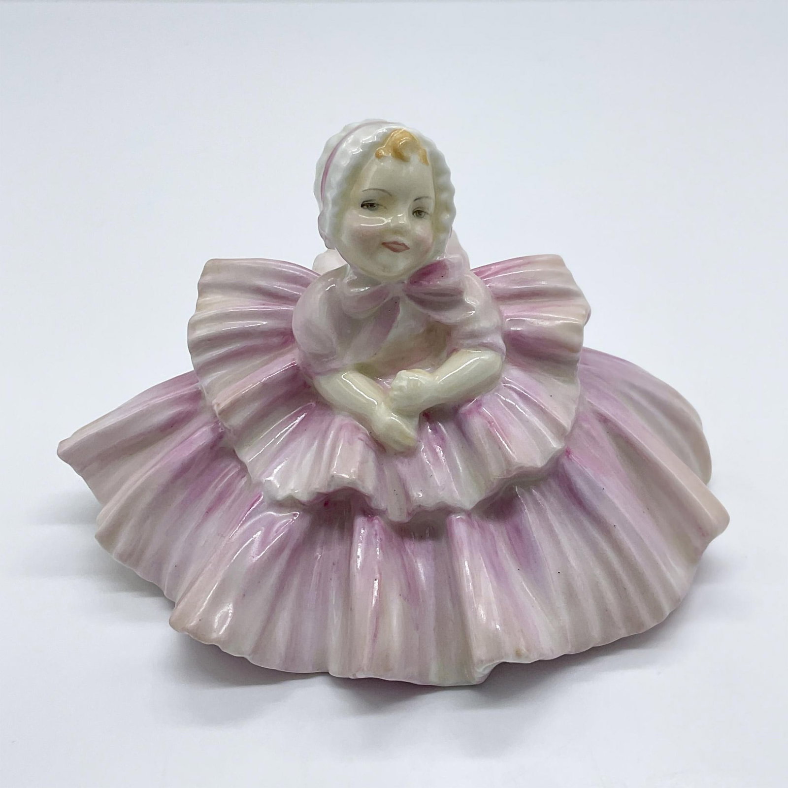 Royal Doulton Figurine, Rosebud HN1580: A precious figure of a very small girl in a big ruffled dress wearing a matching bonnet. Part of the Harradine Child Classics Collection. Royal Doulton backstamp. Artist: Leslie Harradine Issued: 1933