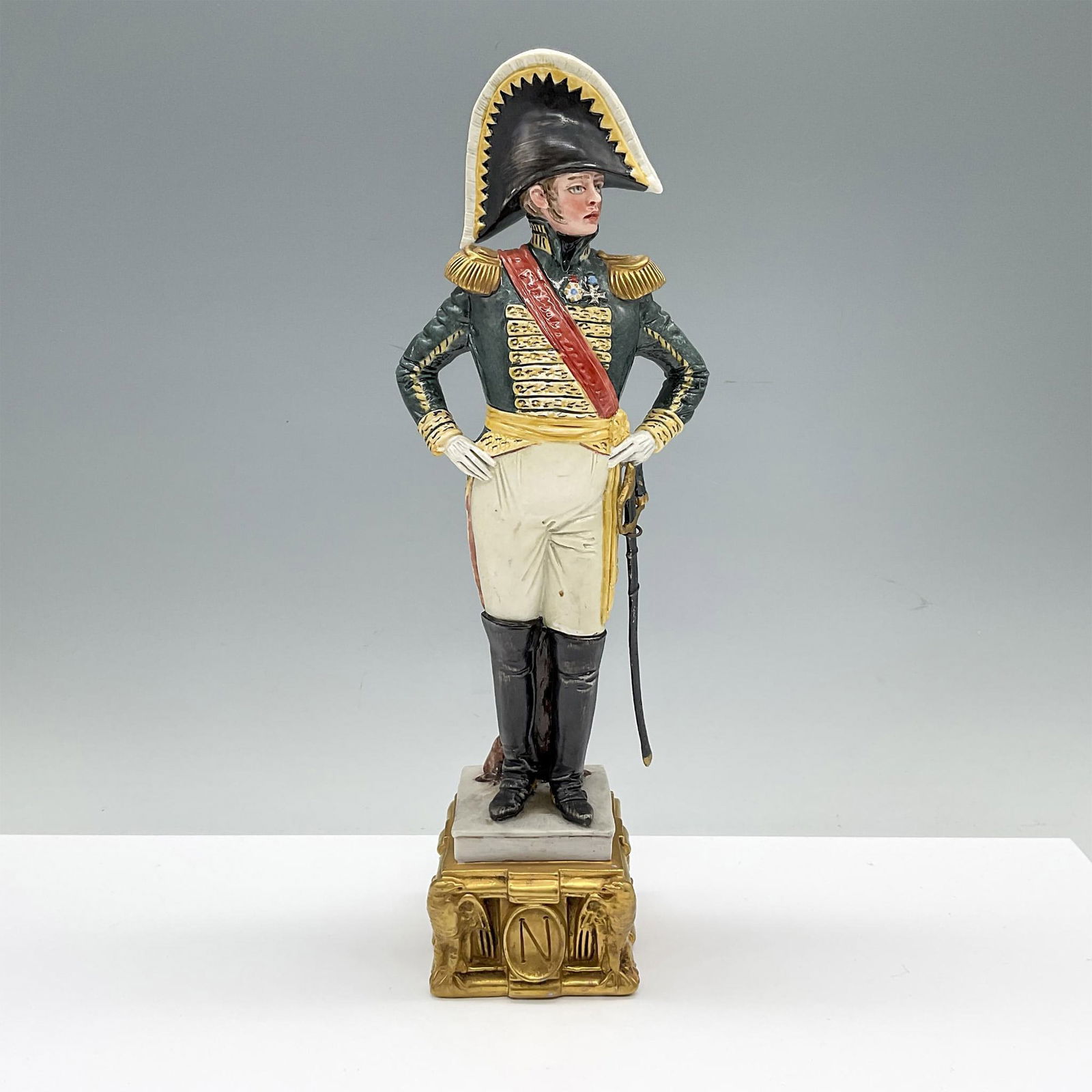 Capodimonte by Bruno Merli Porcelain Soldier Figurine: Hand painted and hand modeled military figure in dressed uniform. He is shown in a bicorn hat and hands on his hips. He is attached to a gilded base with a N marked on the front. The sword sways on hi