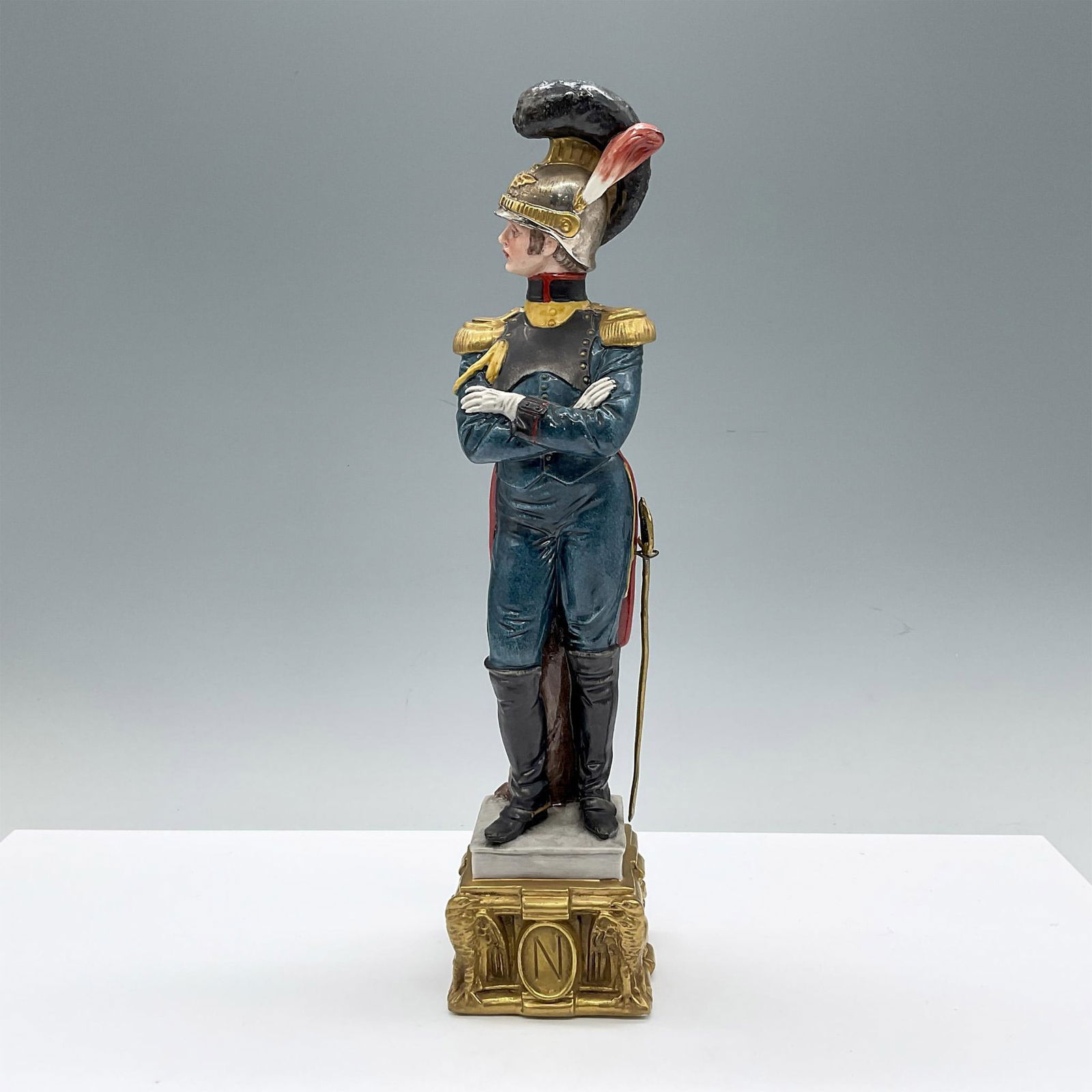 Capodimonte by Bruno Merli Porcelain Soldier Figurine: Hand painted and hand modeled military figure in dressed uniform. He is shown in a silvery-tone helmet, arms crossed over his chest. He is attached to a gilded base with a N marked on the front. The s