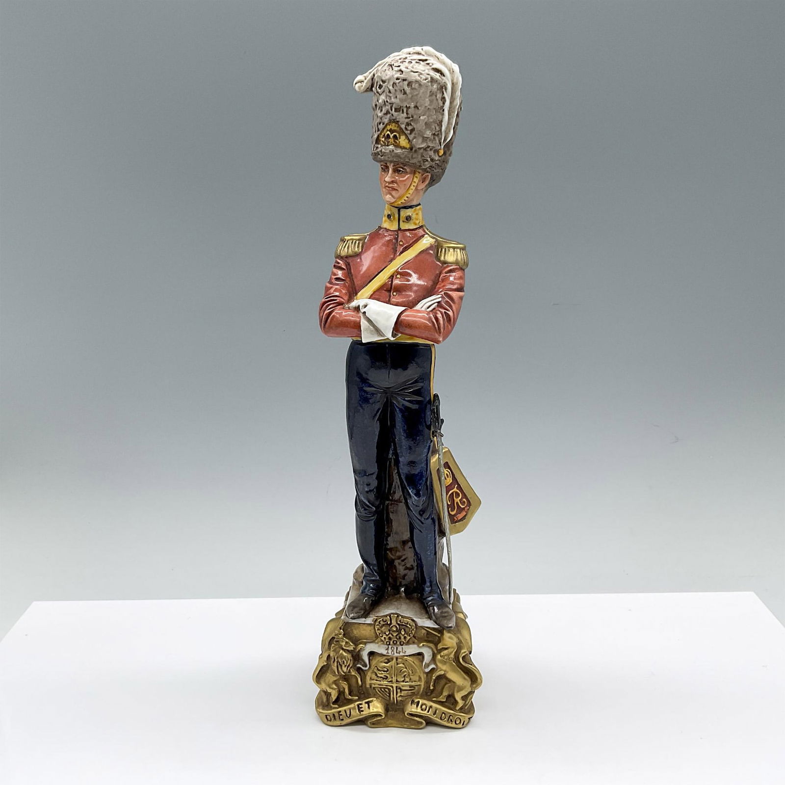 Capodimonte by Bruno Merli Porcelain Soldier Figurine: Hand decorated and hand modeled military figure in dressed uniform. Depicts a man with arms crossed. He is attached to a gilded base marked 1844 over the Coat of arms of the United Kingdom. The sword