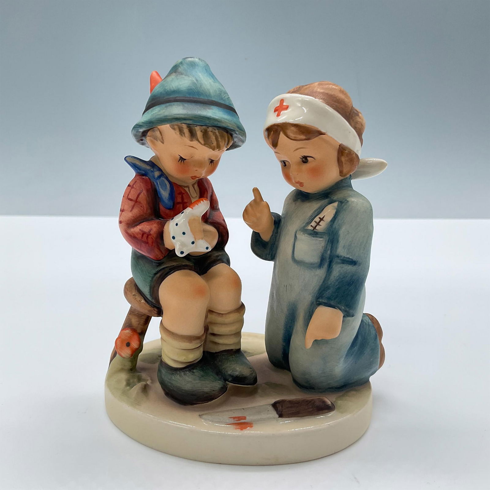 Goebel Hummel Figurine, Little Nurse: Matte porcelain depiction of a little girl making a house call to an injured friend. Goebel backstamp. Issued: 1972 Dimensions: 3.75''L x 2.75''W x 4.25''H Manufacturer: Goebel Hummel Country of Origi