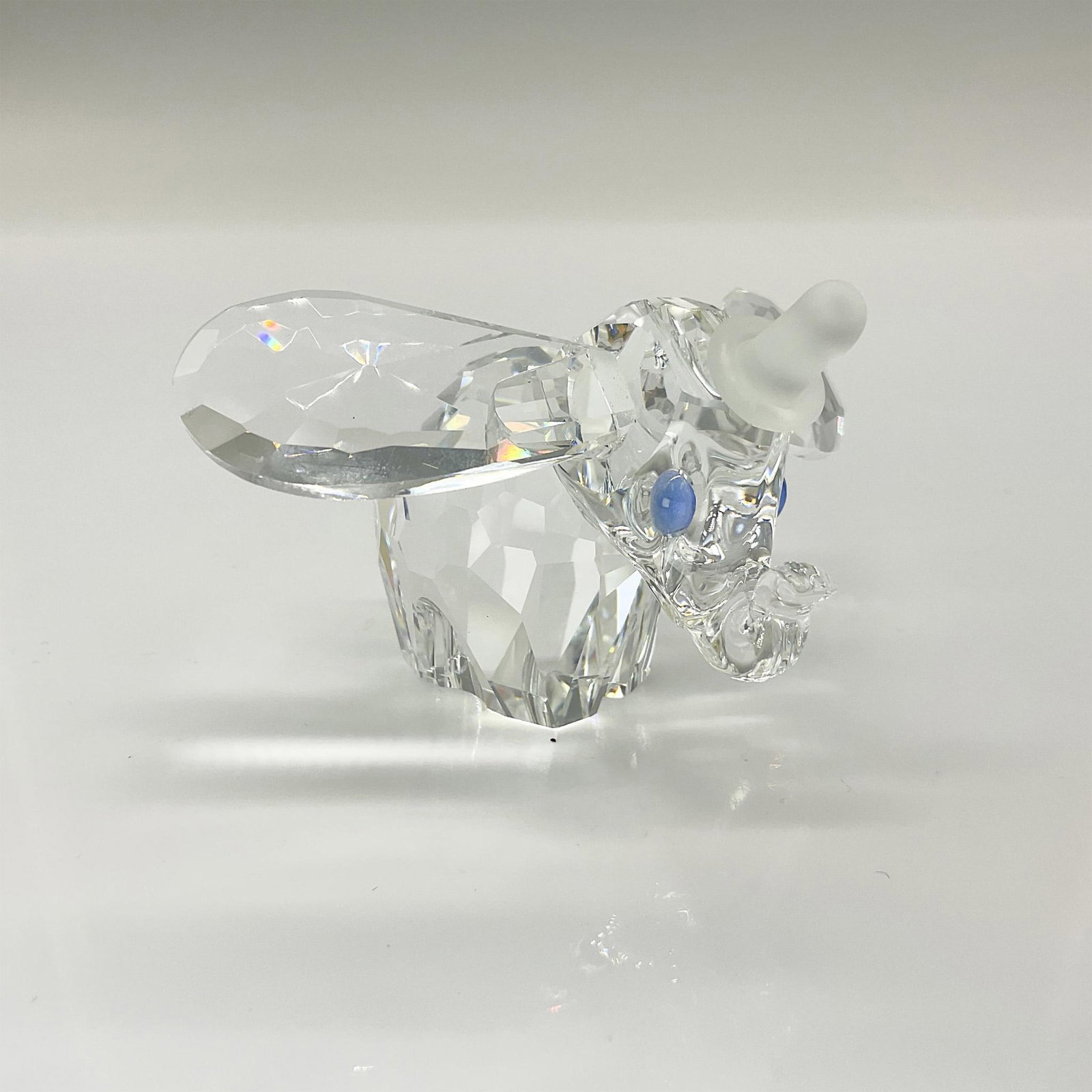 Swarovski Crystal Figurine, Dumbo Hat and Blue Eyes: A clear crystal figure of Dumbo with his ears and trunk raised a bit. Blue crystals are used for the eyes. Swarovski backstamp. This item has its original box. Dimensions of the original box: 6"H x 5"