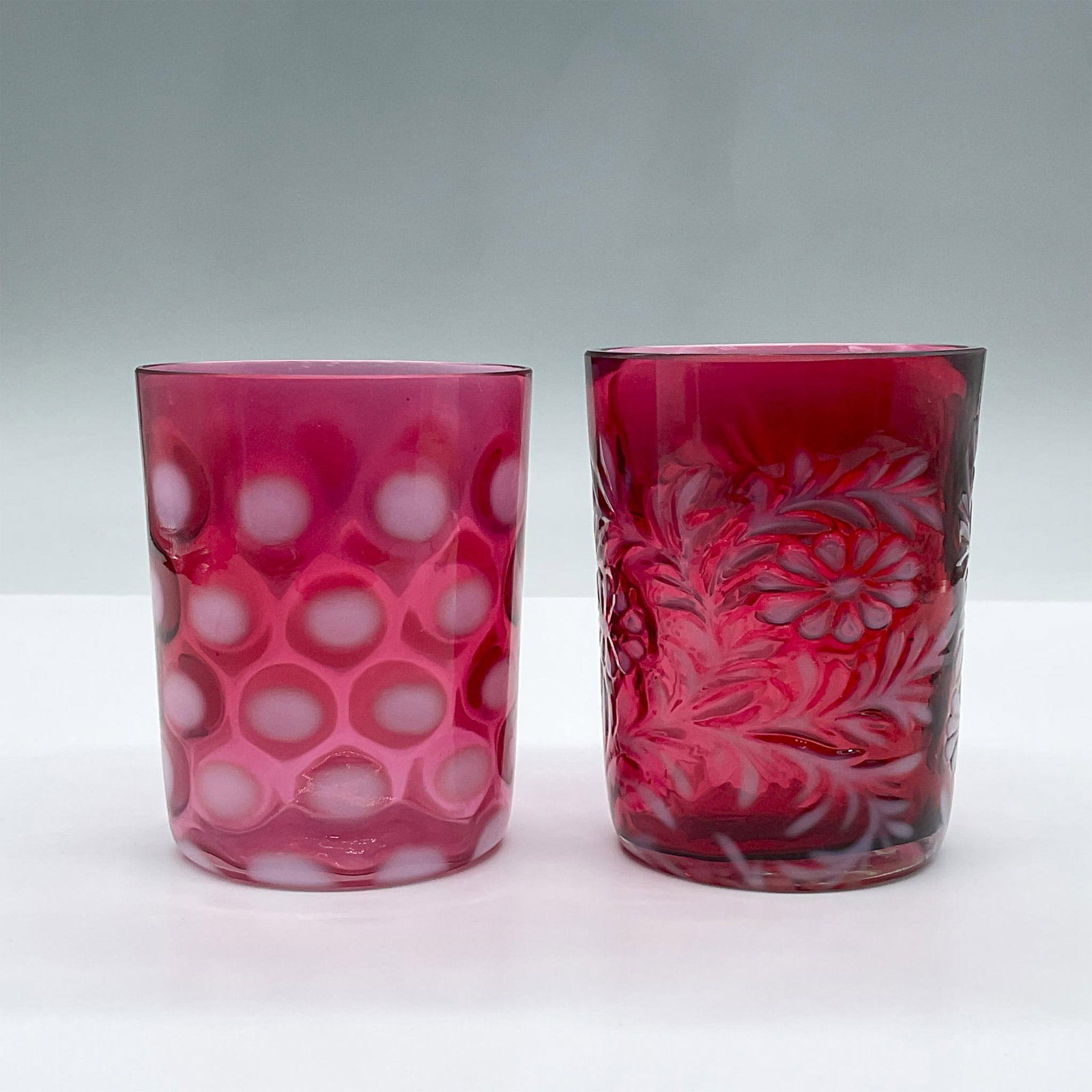 2pc Vintage Fenton Cranberry Glasses: Features two pink short glasses with opalescent designs, one with polka dots and the other with a floral motif. Largest measures 3"L x 3"W x 4"H. Issued: 20th century Dimensions: See Description Manuf