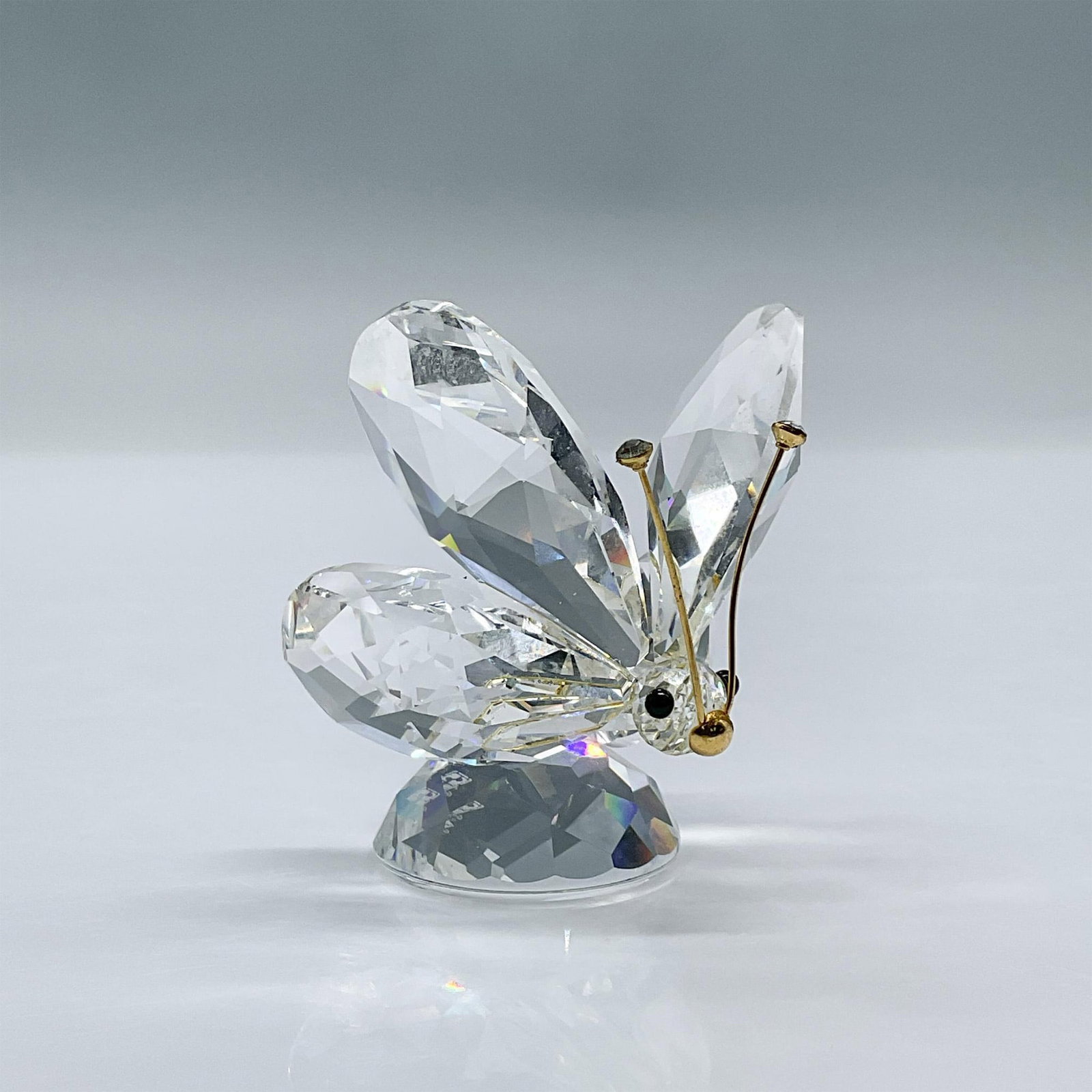 Swarovski Crystal Figurine, Butterfly Gold Antenna: Features a faceted clear crystal body with black eyes and gold antennae with crystal tips. This item has its original box measuring 4''H x 5''dia. Swarovski acid mark. 010002. Issued: 1986 - 2006 Dime