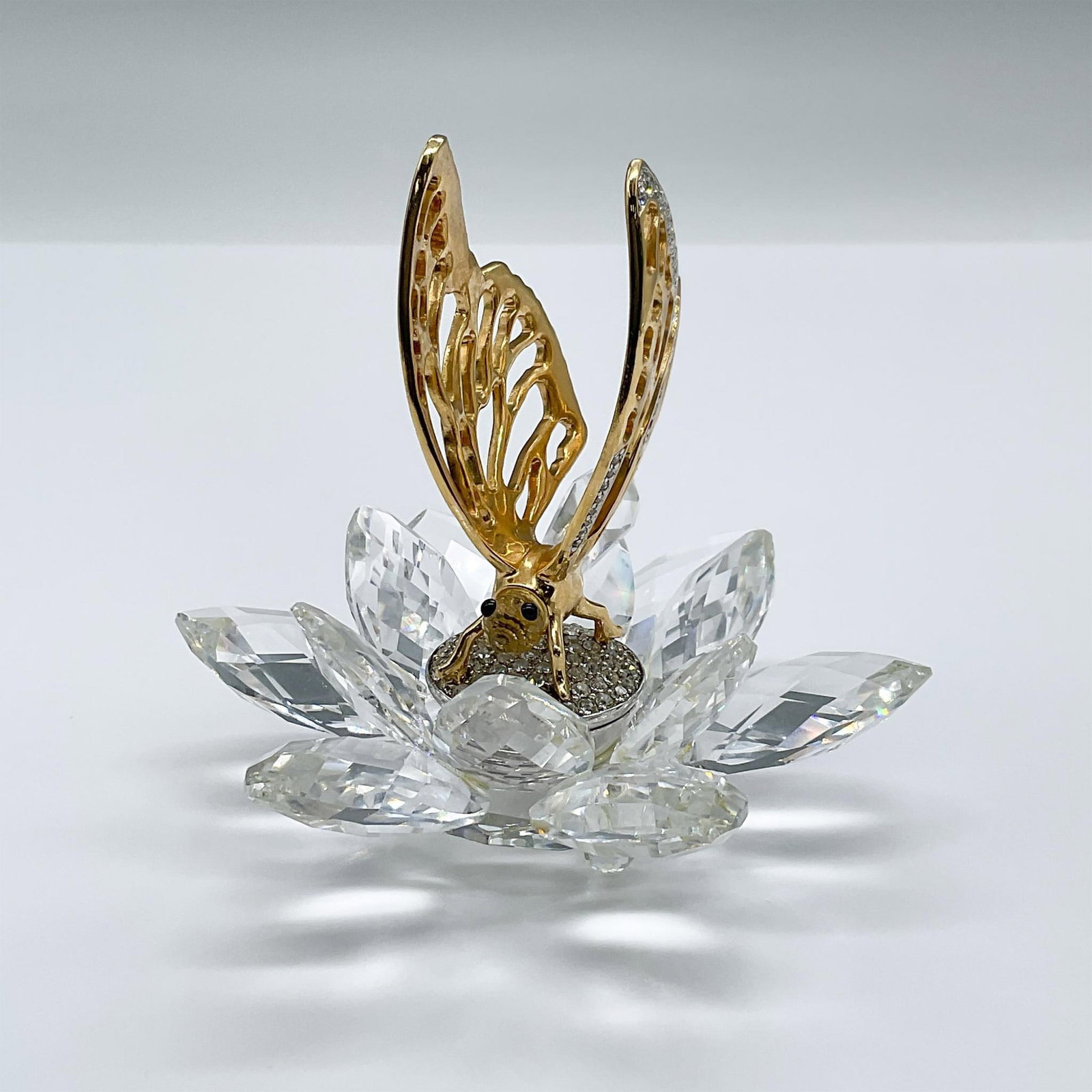 Swarovski Crystal Figurine, Gold Butterfly In Flight: This figure is one of 6 members of the In Flight group. It features a rhodium butterfly and clear faceted crystal flower which makes up the base. This item has its original box measuring 8"H x 6" dia.