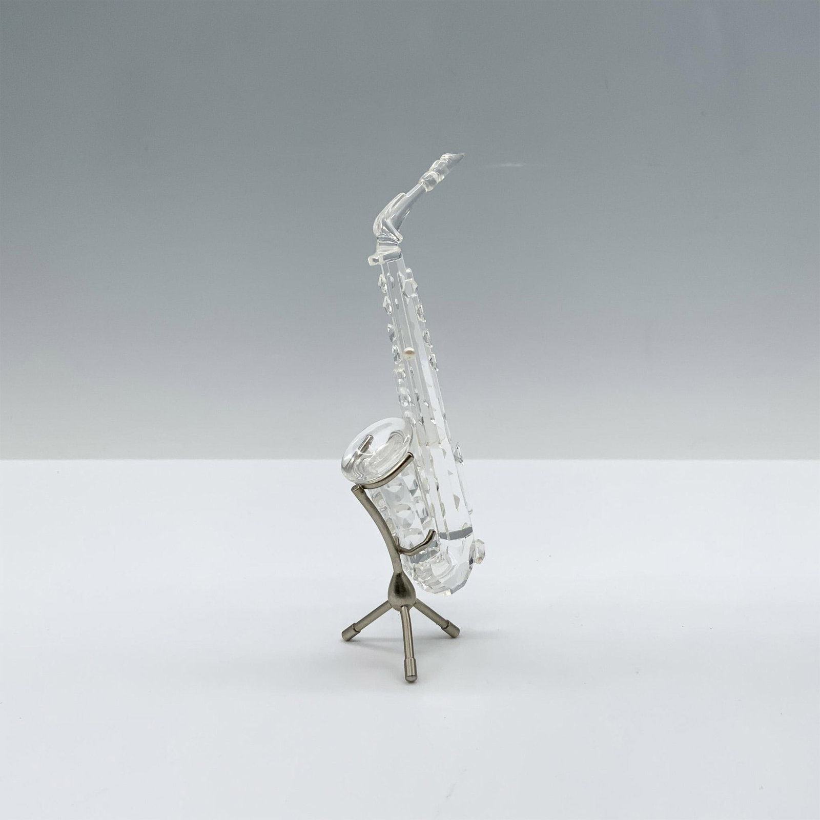 Swarovski Crystal Figurine, Saxophone: Spectacular crystal clear figure that depicts a beautiful saxophone with pearl accents and a rhodium stand. This figure was part of the Crystal Melodies collection. Swarovski backstamp 211728. This it