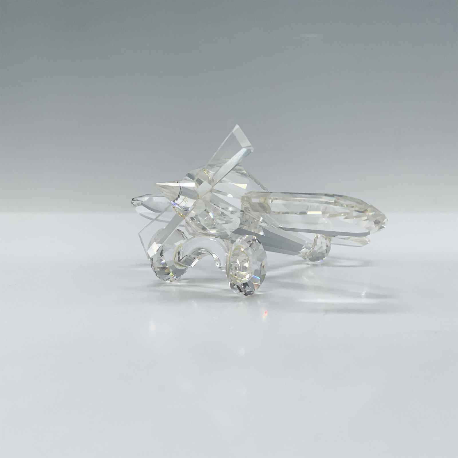 Swarovski Crystal Figurine, Airplane: Beautifully faceted crystal clear depiction of a biplane with a beveled edge propeller. This figure was part of the When We Were Young collection and includes a mirrored base. Swarovski backstamp 1521