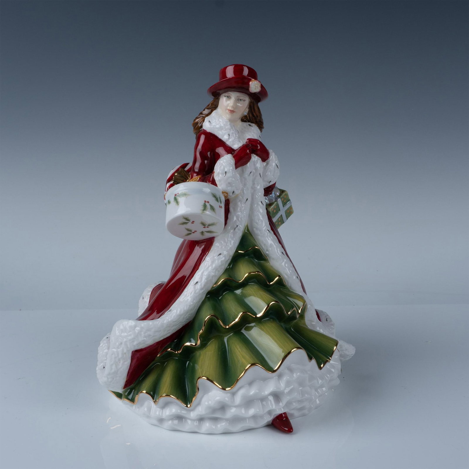 Christmas Day 2010 - HN5379 - Royal Doulton Figurine: Hand decorated bone china figurine from the Pretty Ladies series. Depicts a woman in a red overcoat and hat walking with presents in hand. 22k gold detailing. Royal Doulton backstamp. Signature in gol