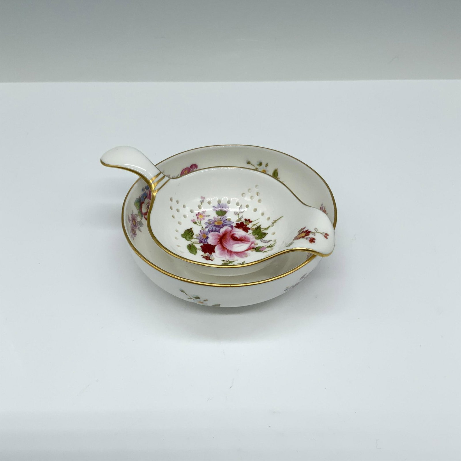 2pc Royal Crown Derby Tea Strainer and Bowl, Derby Posies: Bone China tea strainer and matching under bowl in the Derby Posies Pattern. Both pieces have a white background and are wonderfully decorated with floral sprays and a gilt trim. Royal Crown Derby bac