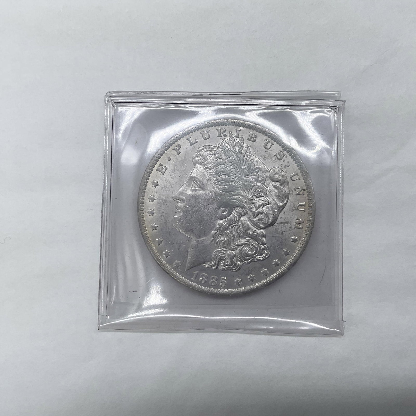 1885-O Morgan Silver Dollar: New Orleans Mint. The obverse side features Liberty in profile. She is shown in cap, flora, and crown. The reverse side depicts an eagle with outstretched wings gripping arrows and an olive branch. Th