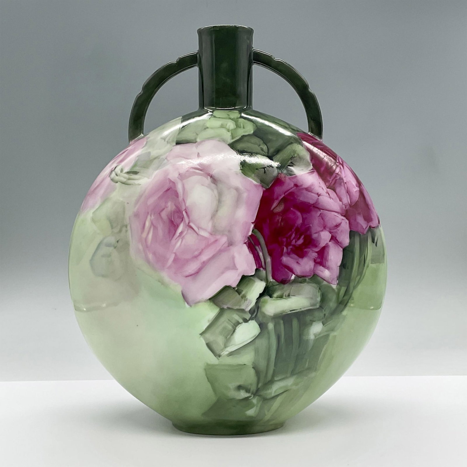 Haviland Limoges Porcelain Double Handle Vase: This vase features a disk like shape with two small handles and a narrow neck. It showcases hand painted pink flowers with green stems against a green background. Haviland backstamp. Issued: 20th cent