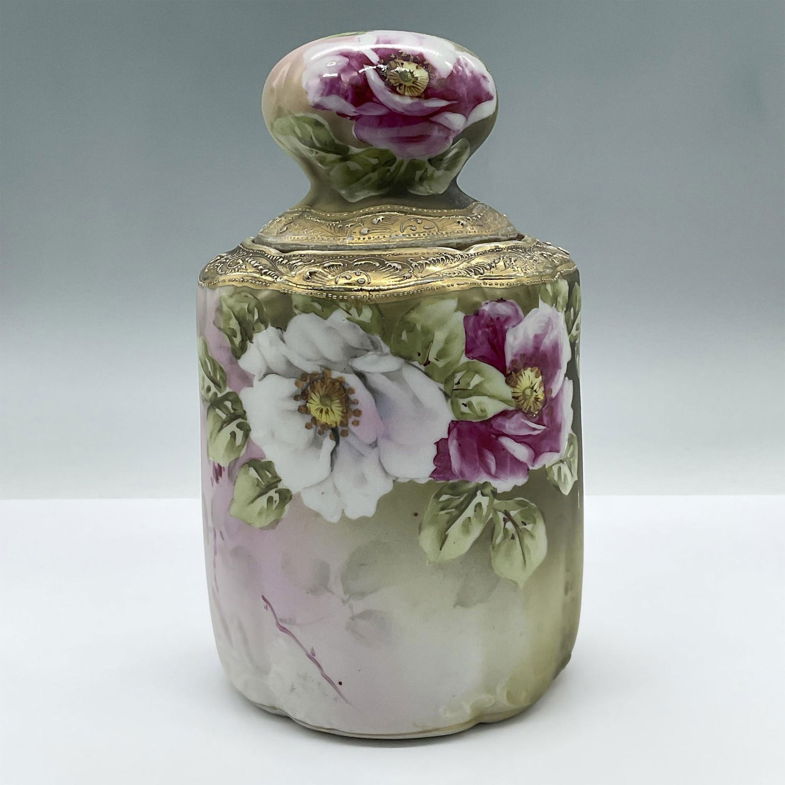 Vintage Nippon Porcelain Lidded Jar: Features a beautifully hand painted jar with a raised lid. It is decorated with glossy flower motifs against a lusterless background and gilded gold details. Marked Nippon. Issued: 20th century Dimens