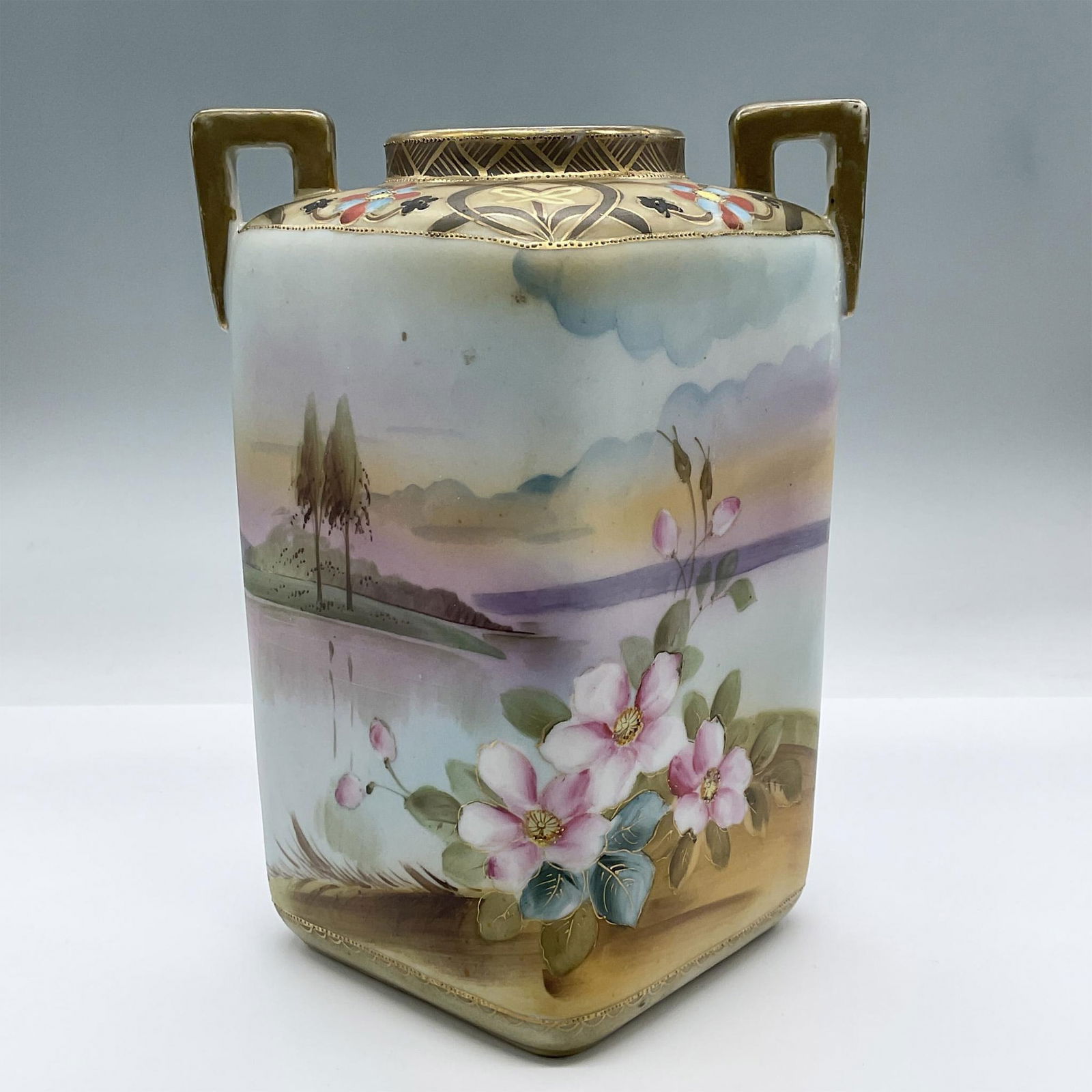 Vintage Nippon Double Handle Porcelain Vase: Features a lovely hand painted landscape scene with trees at the distance and a body of water, decorated with a floral motif and gilded gold details. Nippon backstamp. Issued: 20th century Dimensions: