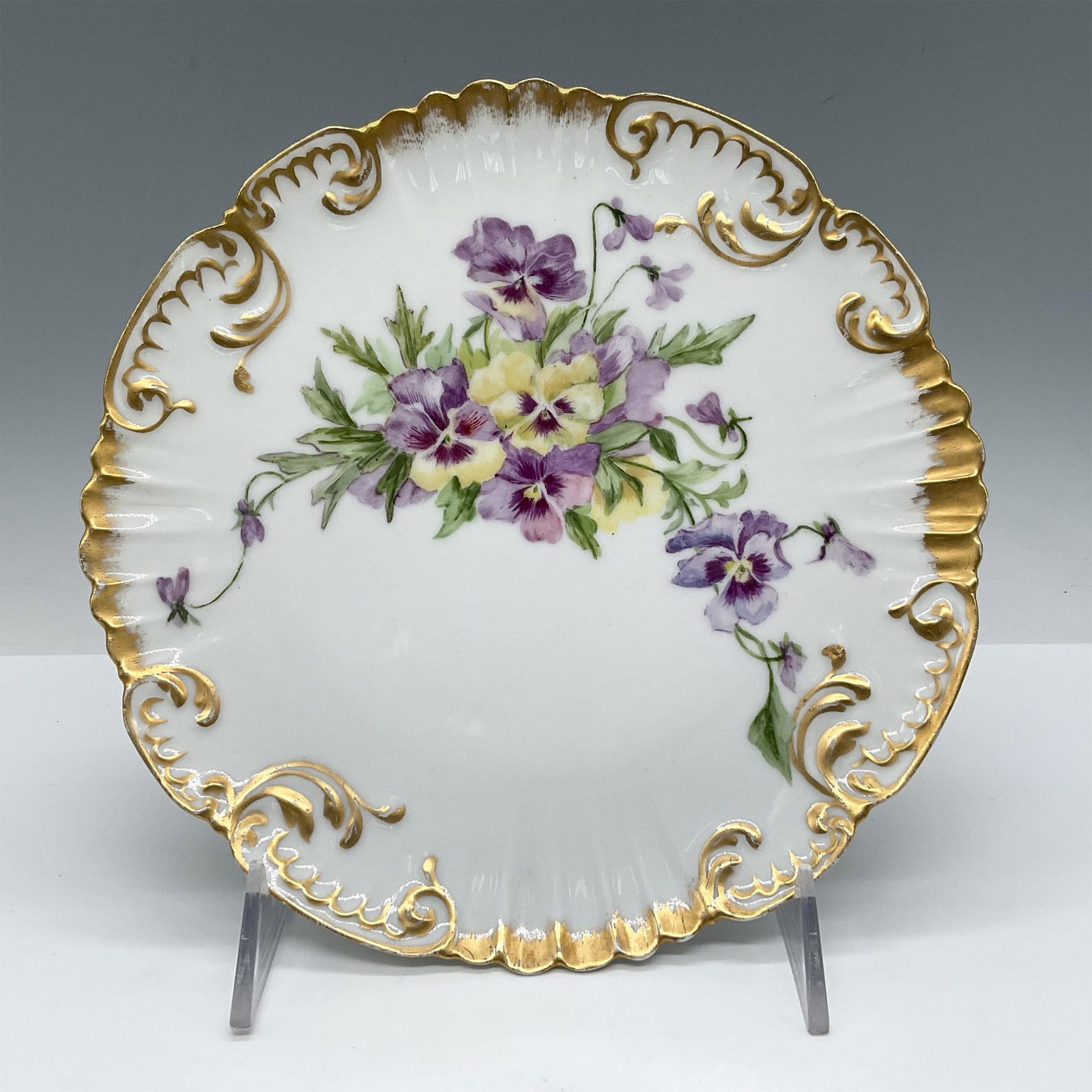 Elite Limoges Porcelain Plate, Pansy: White porcelain with hand painted yellow and purple pansy design. Rim of plate gilt accented. Elite Limoges France backstamp. Issued: 20th century Dimensions: 1"H x 8.5" dia. Manufacturer: Elite Count
