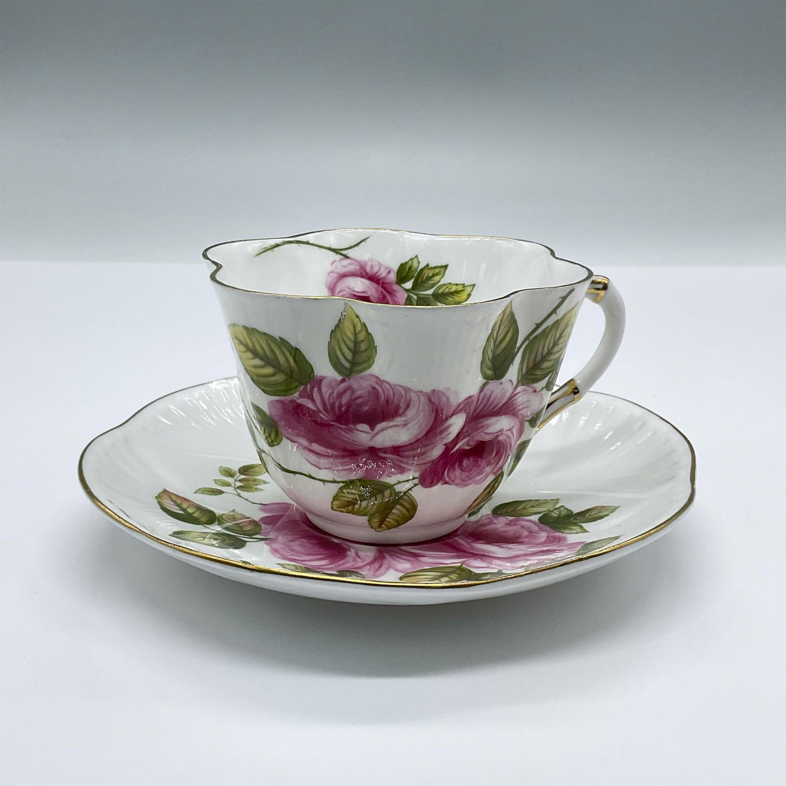 2pc Shelley Fine China Tea Cup and Saucer, Rambler Rose: The cup and saucer feature a pristine white background adorned with their delicate floral Ramble Rose pattern. Both pieces have elegantly scalloped edges accented with a golden trim. Saucer measures 5