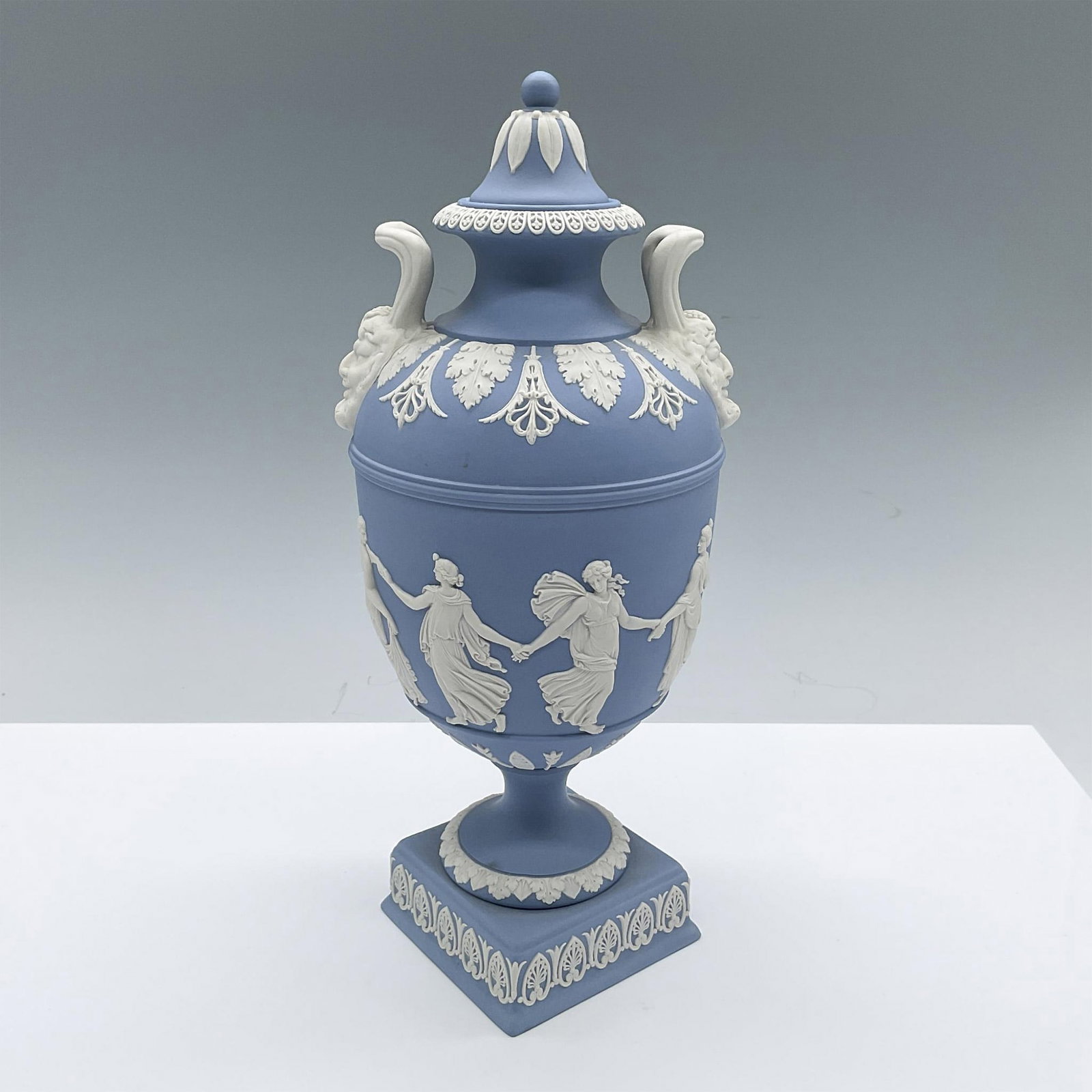 Wedgwood Blue Jasperware Covered Vase, Dancing Hours: Pale blue urn featuring classical motif in white raised reliefs, the Dancing Hours. Wedgwood Made in England impressed on the base. Issued: 20th century Dimensions: 5"L x 4.75"W x 10.5"H Manufacturer: