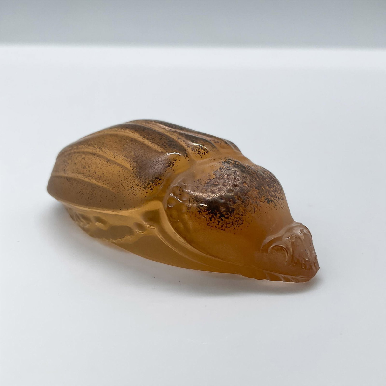 Lalique Art Glass Figurine, Scarabee Meloe Orange Bronze: Art glass insect display figurine. This scarab beetle is made from orange tinted glass with bronze dusting on top. Lalique France etched backstamp. Dimensions: 1.25"L x 2.25"W x 0.75"H Manufacturer: L