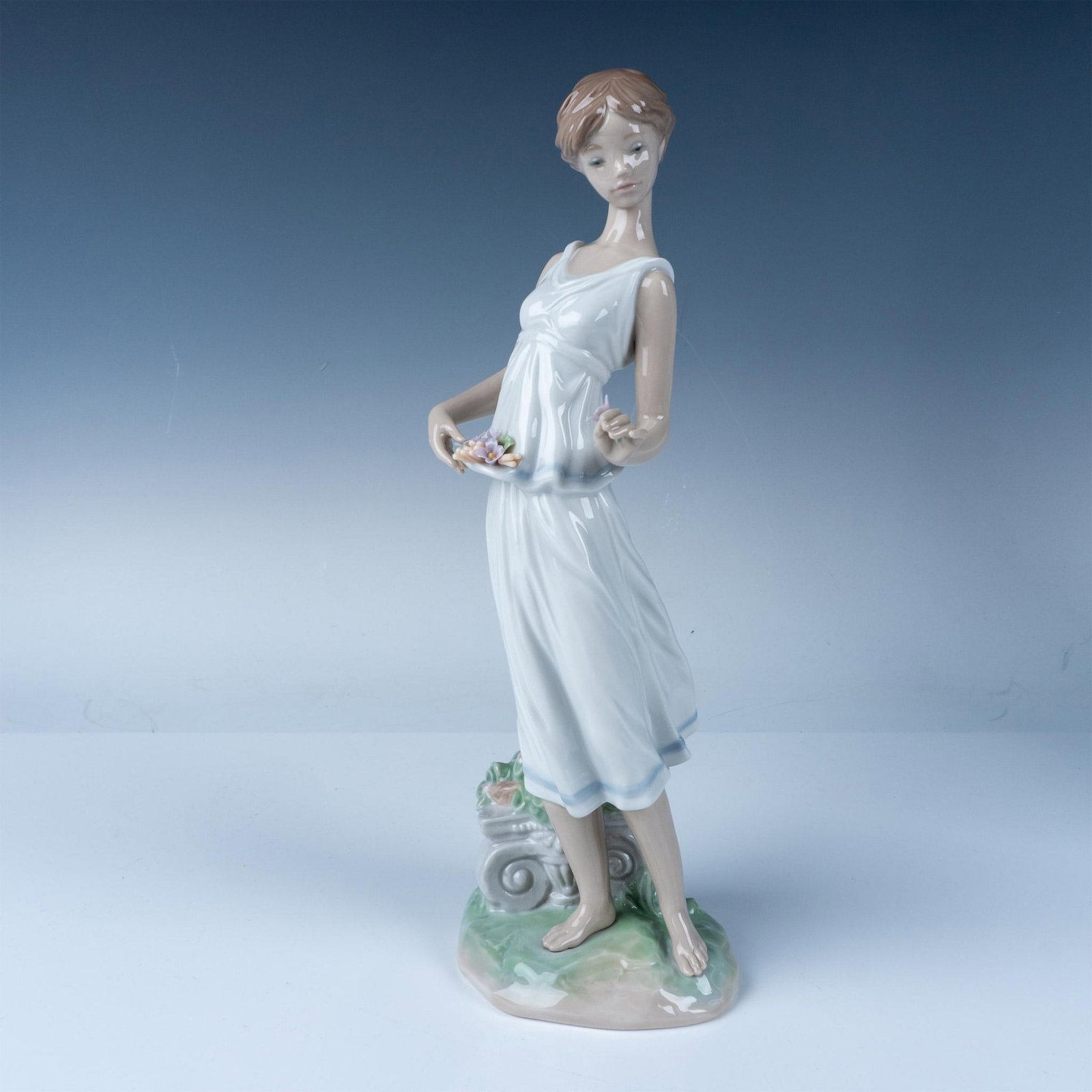 Lladro Porcelain Figurine Flowers for a Goddess 7709: Lladro Flowers for a Goddess figurine, model number 07709, depicts a graceful woman holding delicate pastel flowers, embodying timeless beauty and elegance. Designed by Jose Puche and introduced in 20