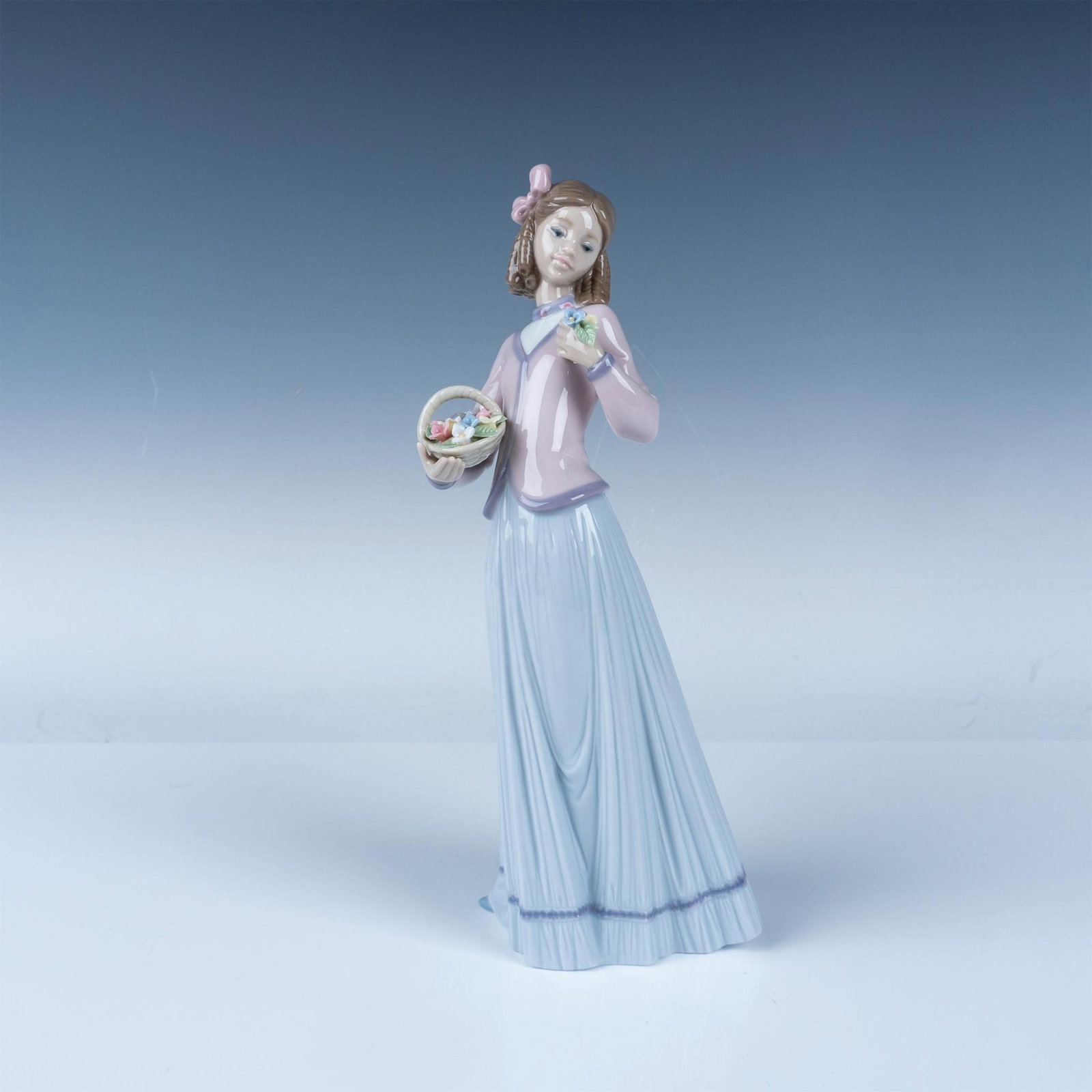 Lladro Porcelain Figurine Girl with Basket of Flowers: A fine Lladro porcelain figurine depicting a young girl holding a basket of flowers, delicately adorned with pastel colors and intricate floral detailing. The figurine highlights Lladro's signature cr
