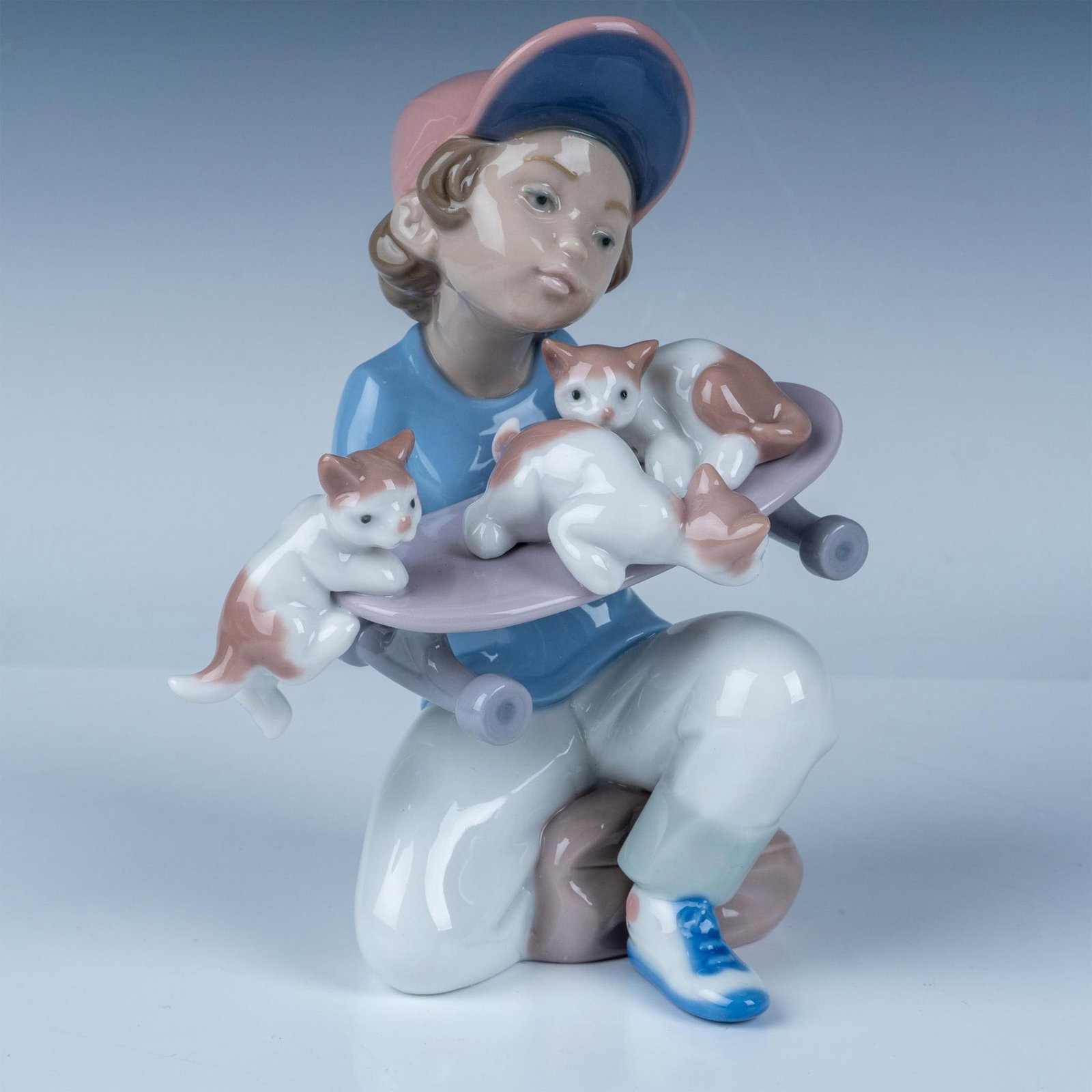 Lladro Porcelain Figurine Little Riders No. 1007623 with Box: This delightful Lladro porcelain figurine, titled Little Riders (No. 1007623), depicts a young boy kneeling as he gently balances three playful kittens on a skateboard. The piece, sculpted by Salvador