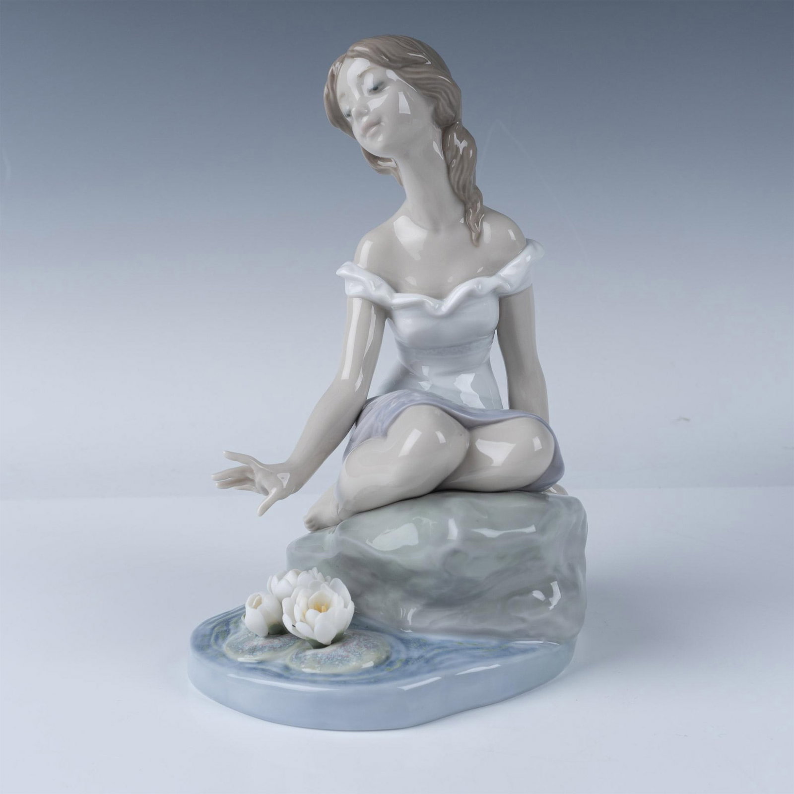 Lladro Porcelain Figurine Reflections of Helena 7706: Lladro Reflections of Helena figurine, model number 07706, depicts a serene woman seated beside a tranquil pond, surrounded by delicate water lilies. Sculpted by Jose Luis Alvarez and introduced in 20