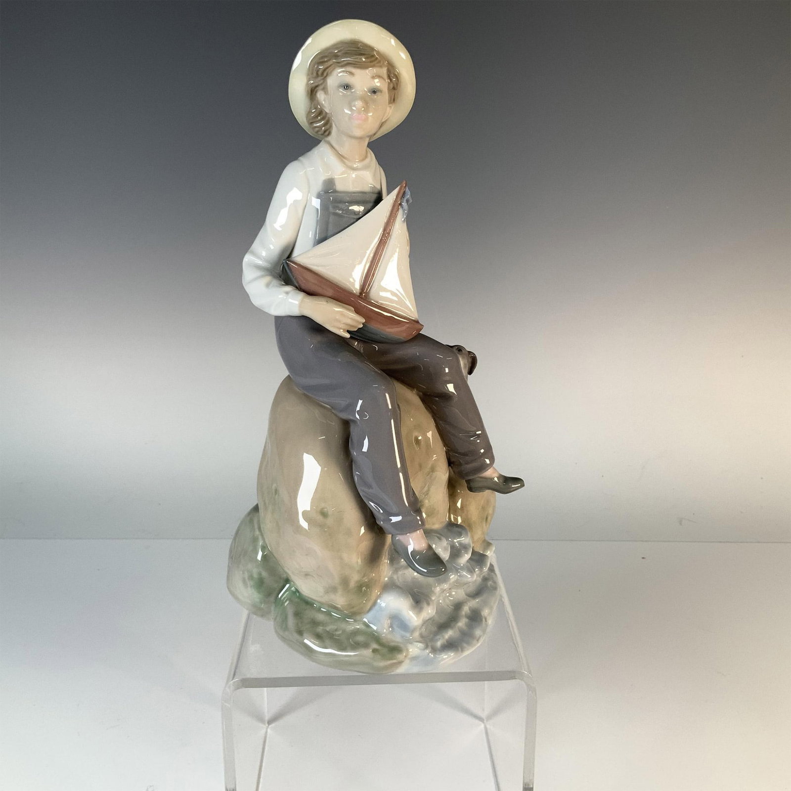 Lladro Porcelain Figurine Sea Fever 1005166: This Lladro porcelain figurine, titled "Sea Fever," features a young boy gazing longingly with a nautical theme. Model number 1005166, the piece is finished in a glossy glaze and bears the official Ll