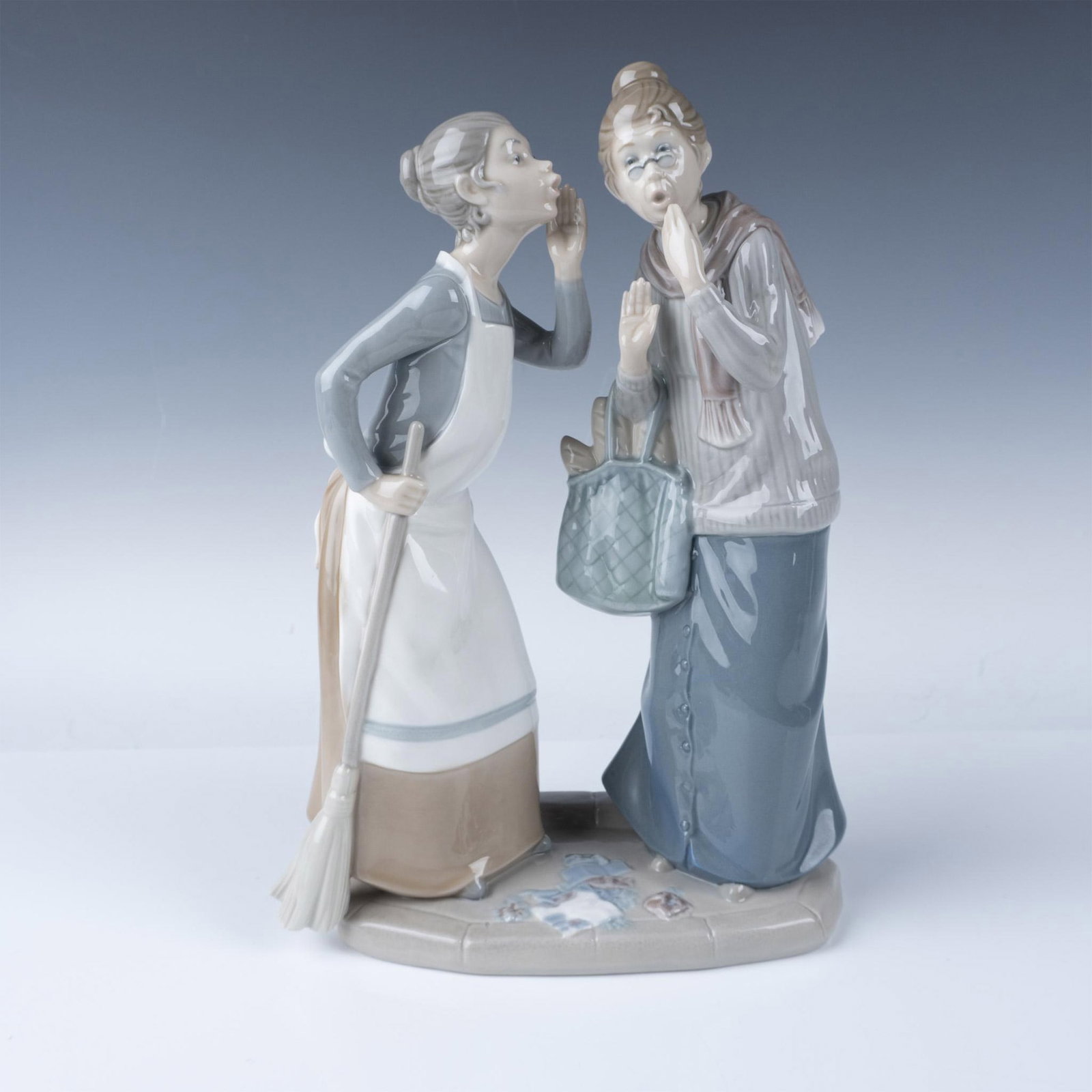 Lladro Porcelain Figurine The Gossips 1004984: This glossy figure depicts two women engaged in a whispered conversation as they model soft pastel hues and intricate detailing, capturing the delicate expressions, flowing garments, and lifelike pose