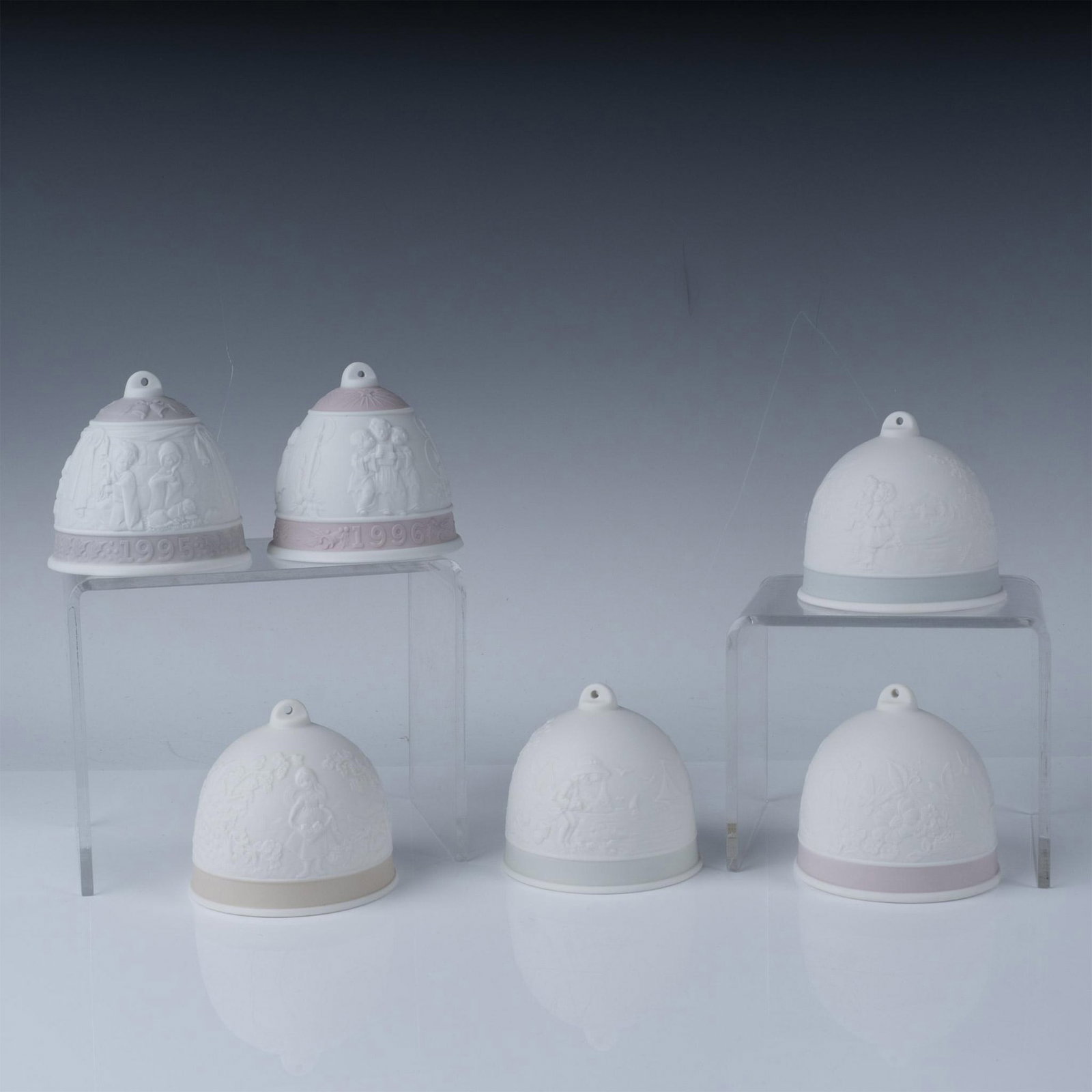 6pc Lladro Porcelain Collector Bells: A set of six Lladro porcelain collector bells, featuring intricate bas-relief designs depicting various seasonal and festive scenes. Each bell is finely crafted with a matte white finish and delicate 