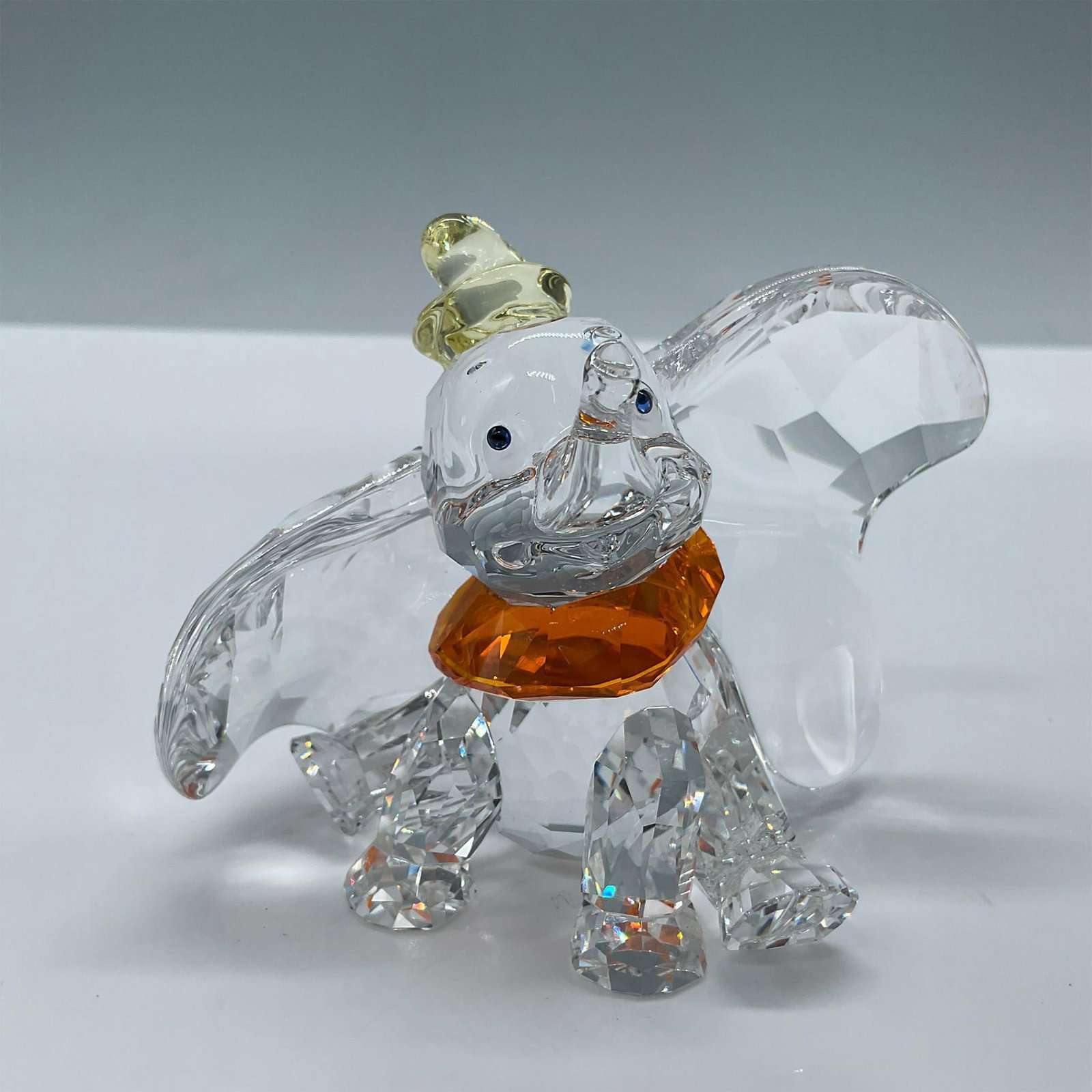 Swarovski Crystal Figurine, Disney Dumbo: Adorable clear crystal dumbo with jonquil hat and light sapphire eyes. Includes the original box, dimensions: 6''L x 6''W x 4''H. Swarovski etched backstamp. Issued: 2011 Dimensions: 3.5''L x 2.5''W x