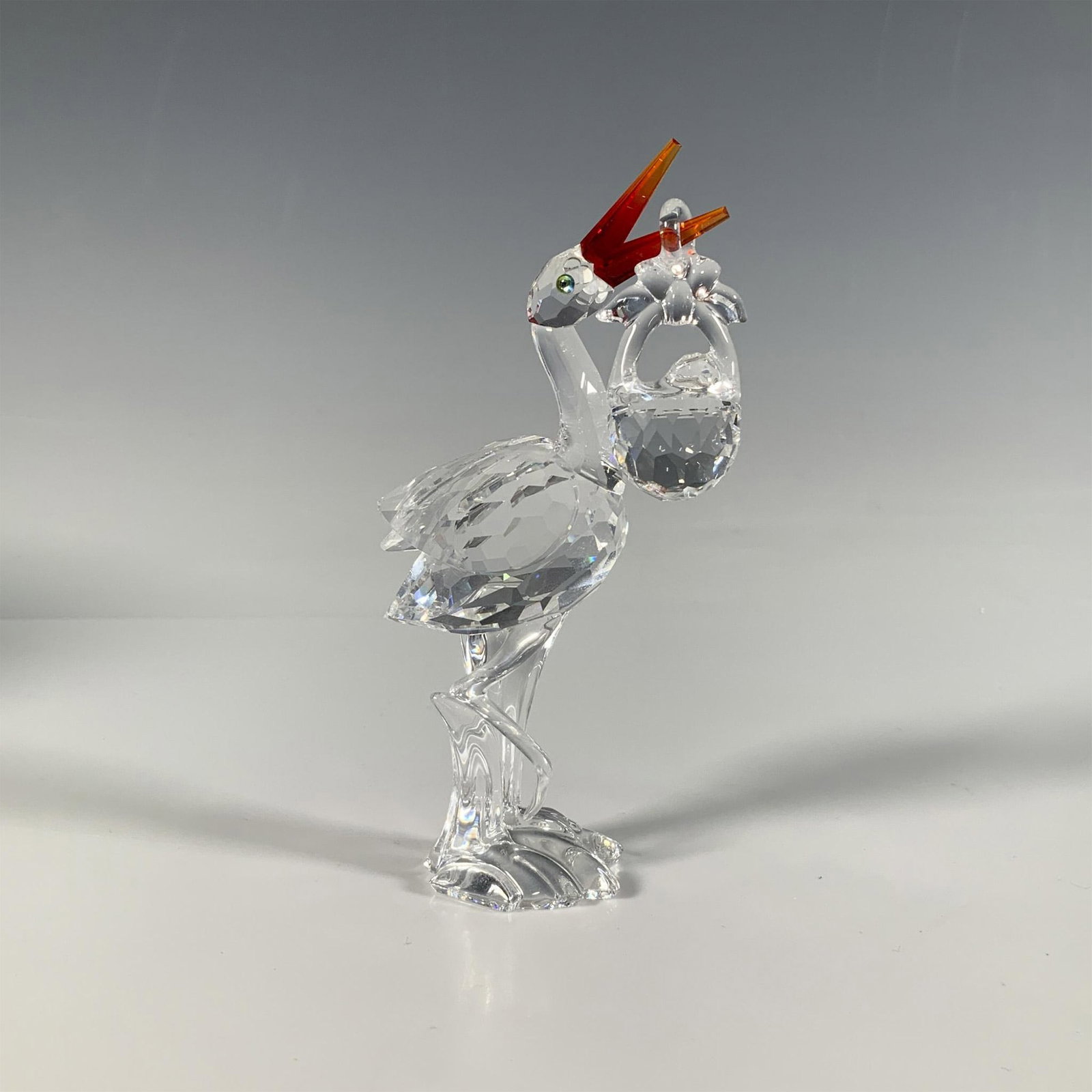 Swarovski Crystal Figurine, Stork with Baby: A precious faceted crystal figure of a stork carrying a baby on its bright red beak. Part of the Cheerful Times collection. Swarovski marking. This item has its original box: 6"W x 5"H. Artist: Gabrie