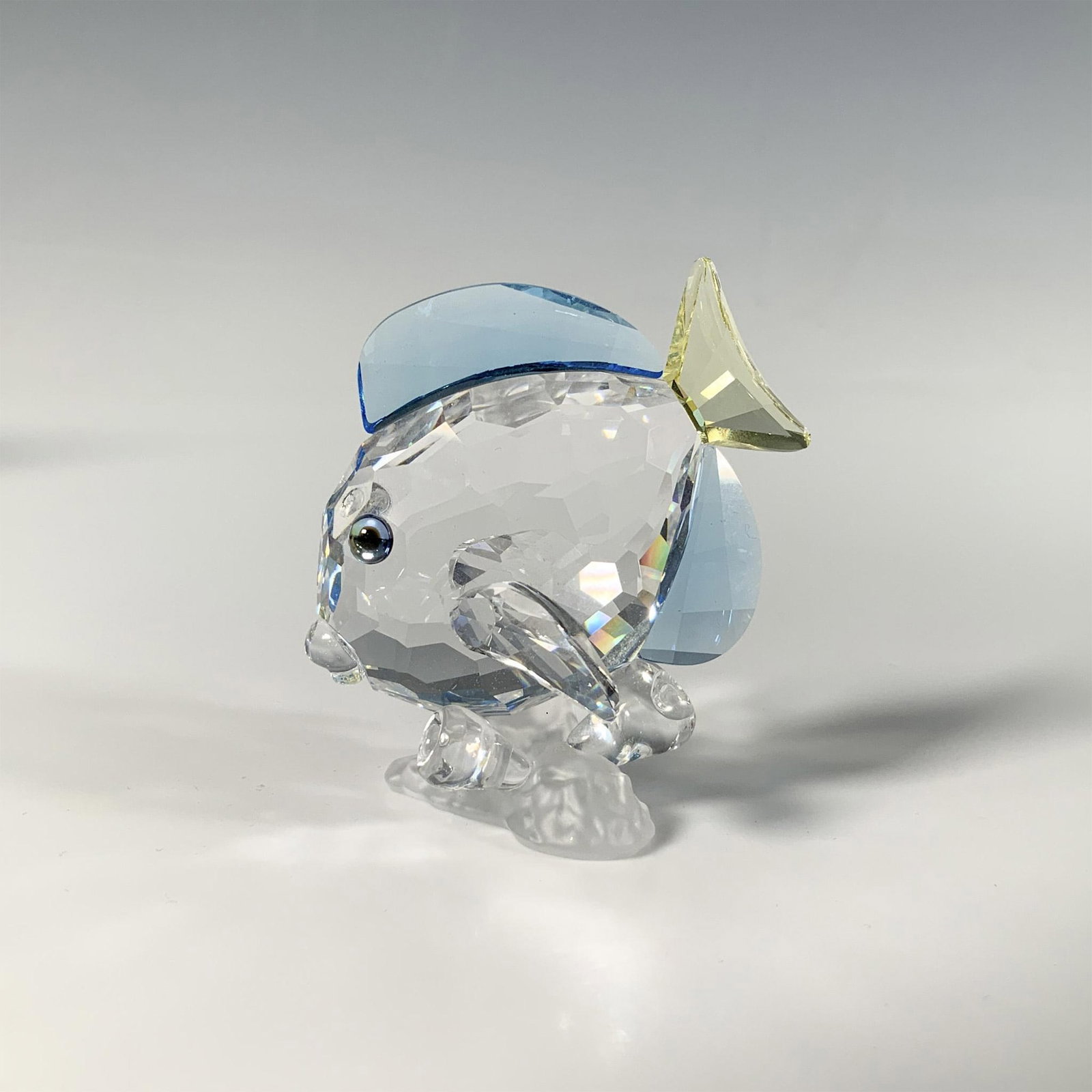 Swarovski Crystal Blue Tang Fish Figurine: A stunning crystal figure, showcasing a detailed fish in clear, blue, and yellow hues, perched atop a frosted coral base. SCS members exclusive. Swarovski marking. This item has its original box: 4.5"