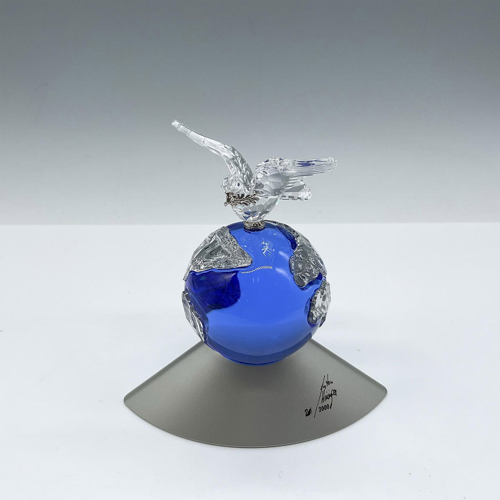 Swarovski Crystal Planet Paperweight, Millenium Edition: Cobalt blue crystal globe with clear crystal continents shown. Bird of peace, dove, holding an olive branch perched on top. Silver toned base signed and dated by artist. Swarovski backstamp. 238985. T