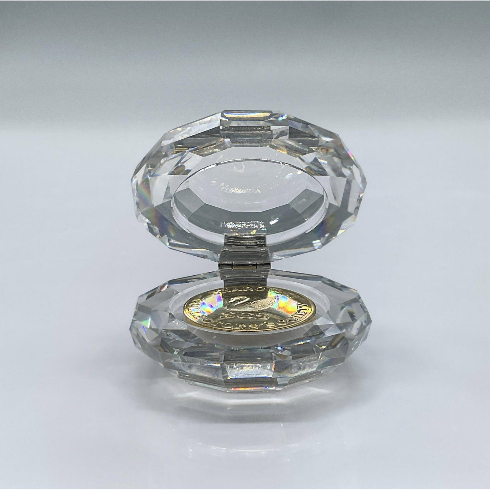 Swarovski Crystal Coin Box With Coin: A faceted clear crystal round box with a golden hinge and golden coin. This item has its original box: 3.25"L x 3.25"W x 2.5"H. Swarovski acid mark. Issued: 1991 - 1995 Dimensions: 2"L x 1.75"W x 1"H 