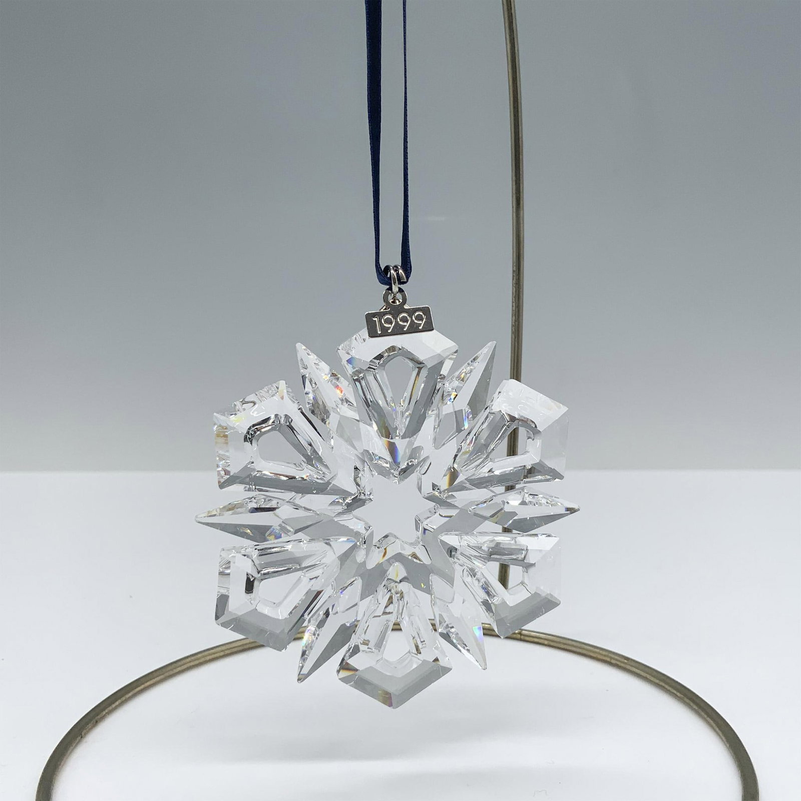 Swarovski Crystal Ornament, 1999 Christmas Ornament: Limited edition crystal ornament with a metal tag reading 1999 as well as 6 kite shaped angles and 6 points that depict a beautiful snowflake design. Swarovski backstamp. 235913. This item has its ori
