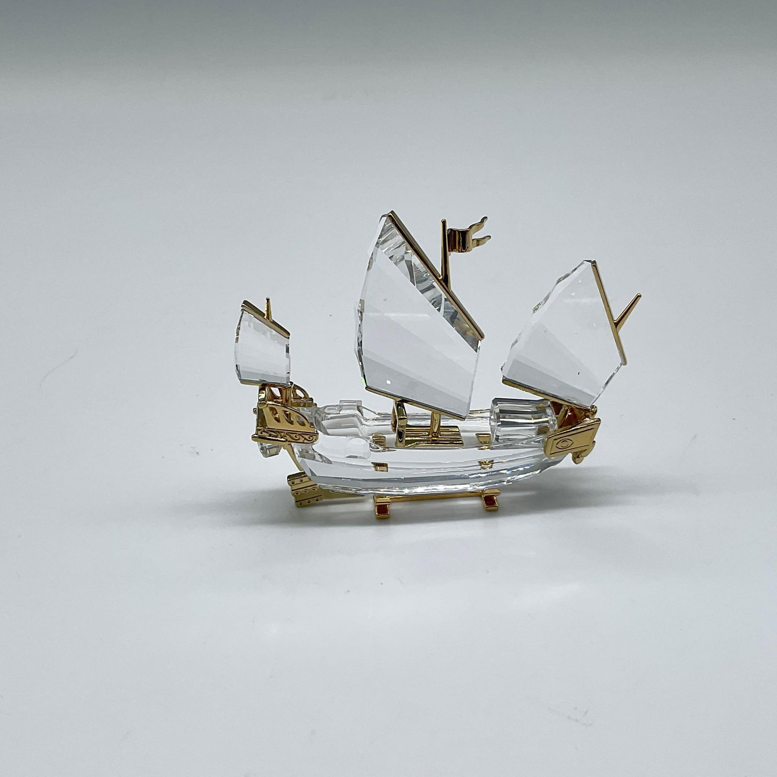Swarovski Crystal Memories Figurine, Chinese Junk: Rare, retired ship is part of the Journeys Theme Group. Clear faceted crystal with gilt metal accents and stand. Swarovski backstamp. 272708. Artist: Team Issued: 2001-2004 Dimensions: 2.5"L x 0.75"W 