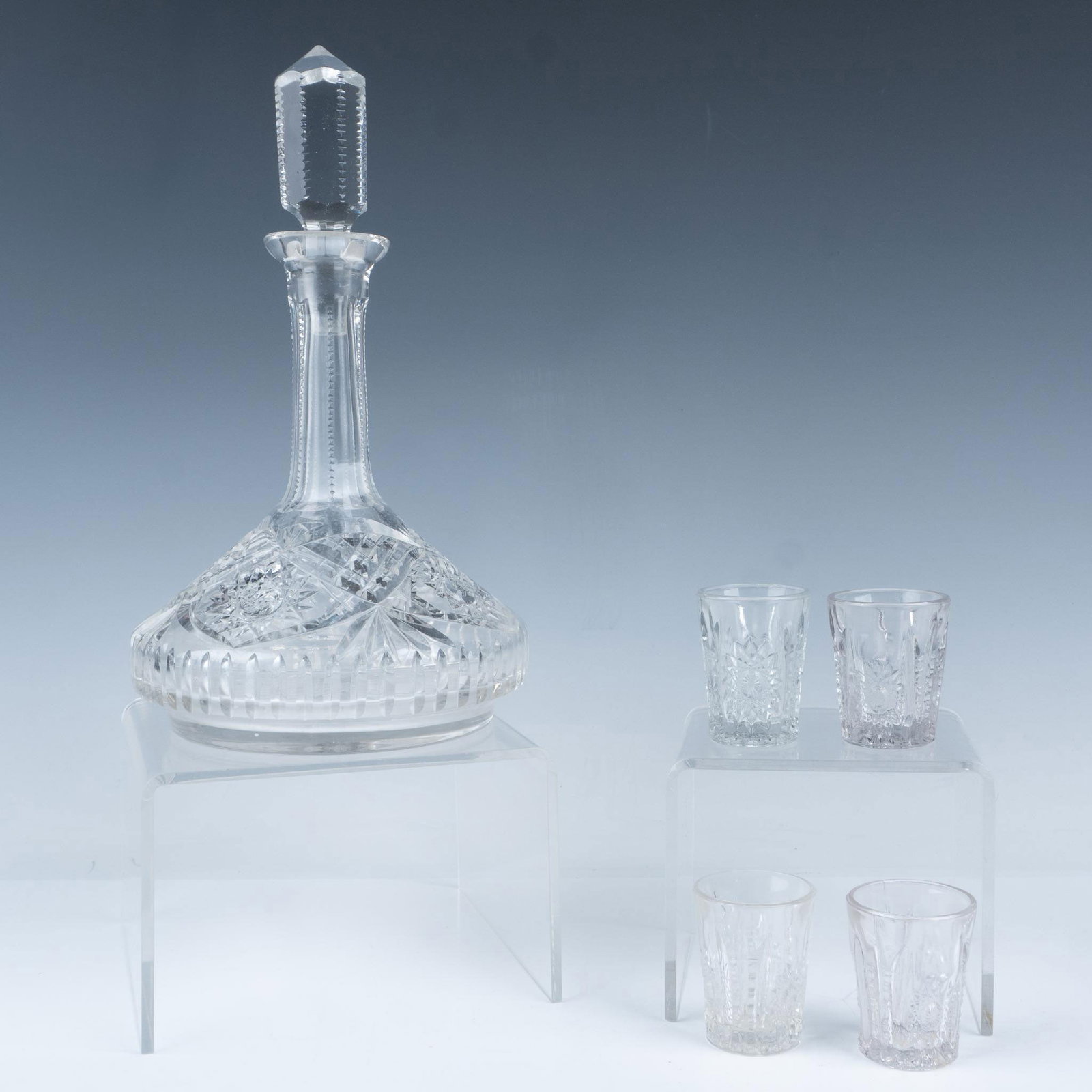 5pc Cut Glass Whiskey Decanter and Shot Glasses: An elegant glass decanter with a stopper and four accompanying shot glasses, featuring a stunning star and vertical cut glass pattern. Decanter dimensions: 6"W x 10.75"H. Glasses dimensions: 1.75"W x 
